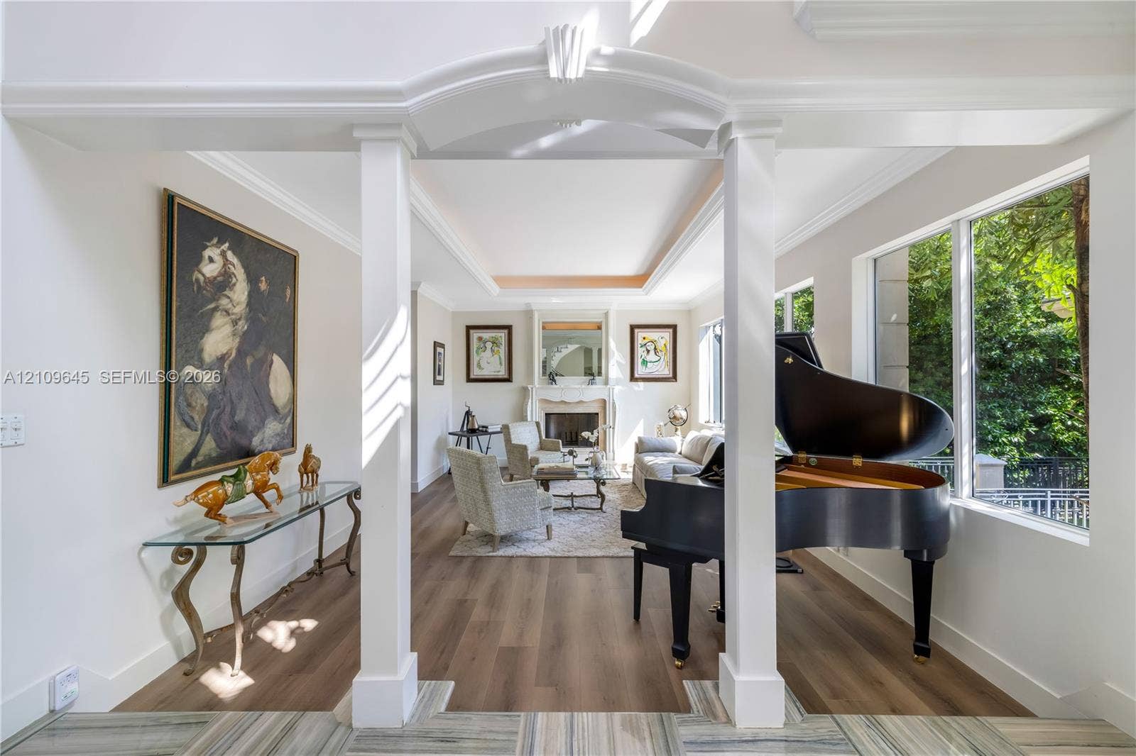 332 Costanera Road, Coral Gables, FL 33143 Open floor plan featuring wood-finish flooring, tray ceilings, a central stone-surround fireplace, and large picture windows