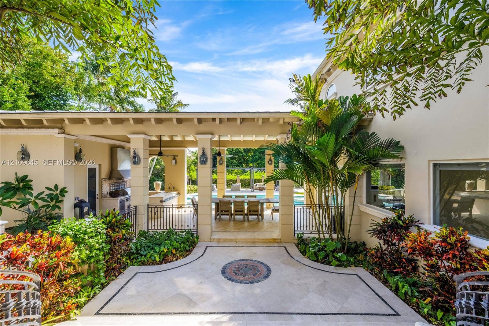 332 Costanera Road, Coral Gables, FL 33143 Covered lanai featuring a stone-paver patio with decorative inlay, built-in outdoor kitchen with stainless steel ventilation hood, and heavy-timber beam ceiling