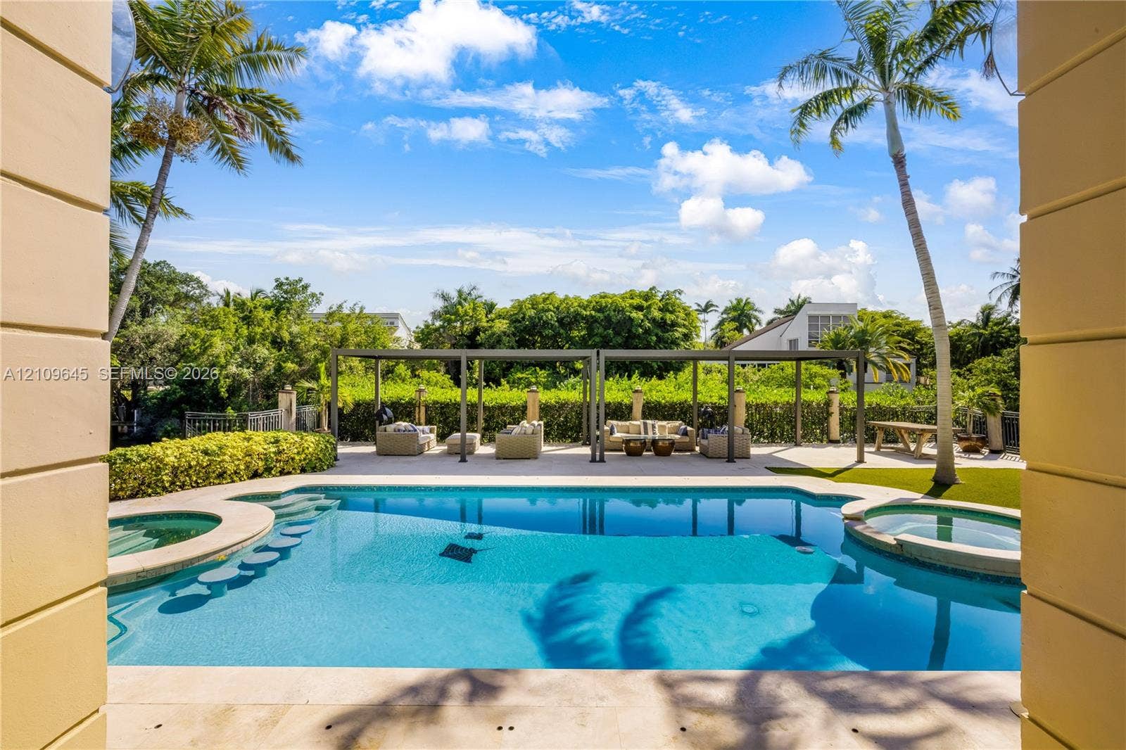 332 Costanera Road, Coral Gables, FL 33143 In-ground pool featuring a sun shelf, integrated spa, and surrounding stone decking, complemented by a metal pergola and mature palm trees
