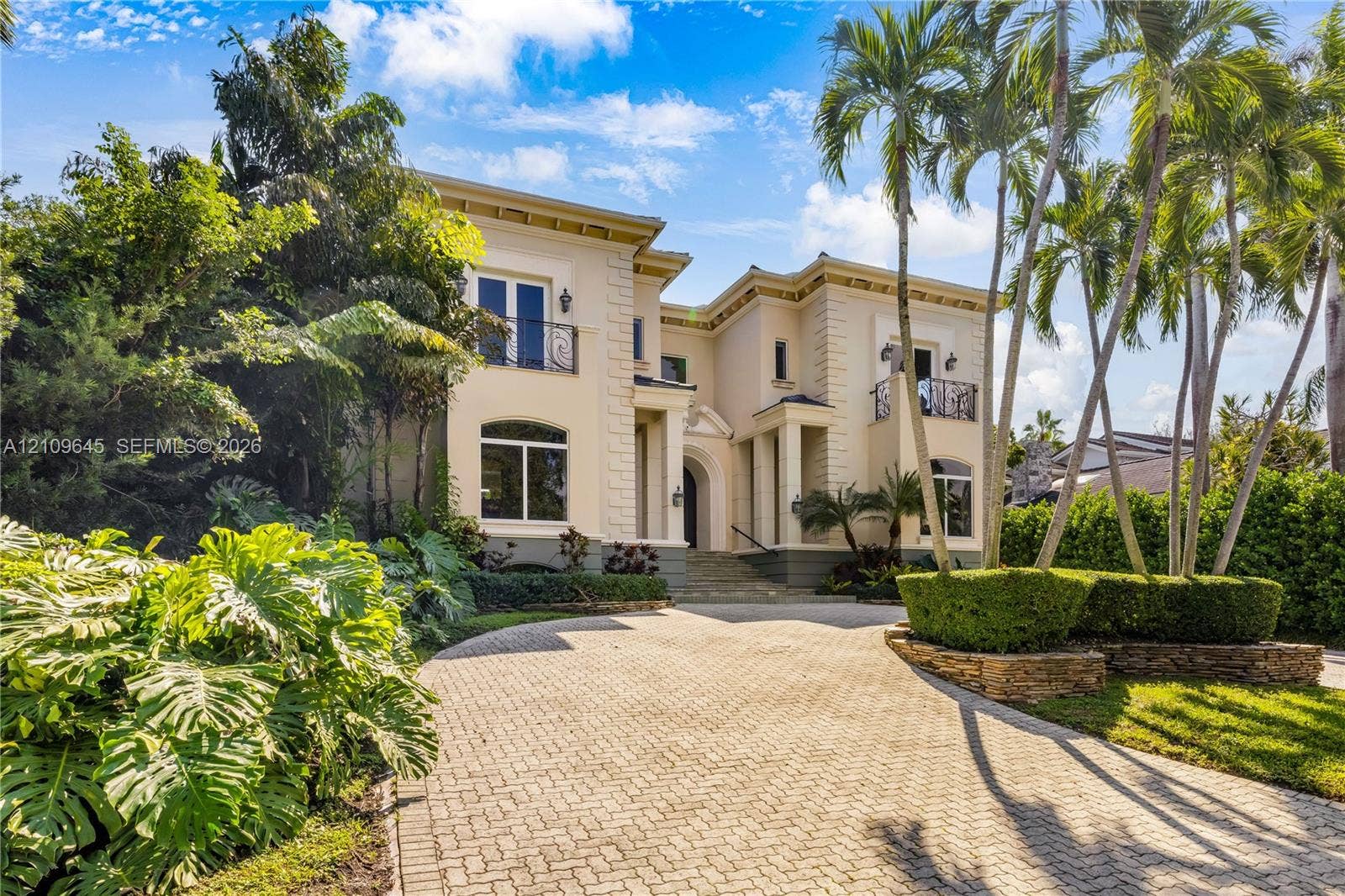 332 Costanera Road, Coral Gables, FL 33143 Two-story exterior featuring a stone-paved circular driveway, wrought-iron balconies, quoined corners, and lush tropical landscaping