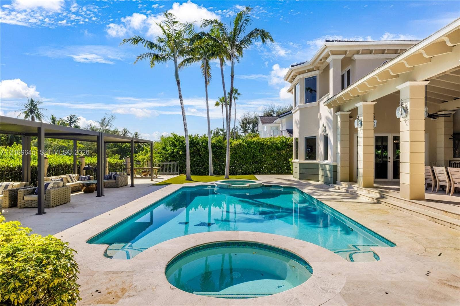 332 Costanera Road, Coral Gables, FL 33143 Outdoor pool with an integrated spa, stone-paver pool deck, covered patio with structural columns, and a detached metal-frame pergola