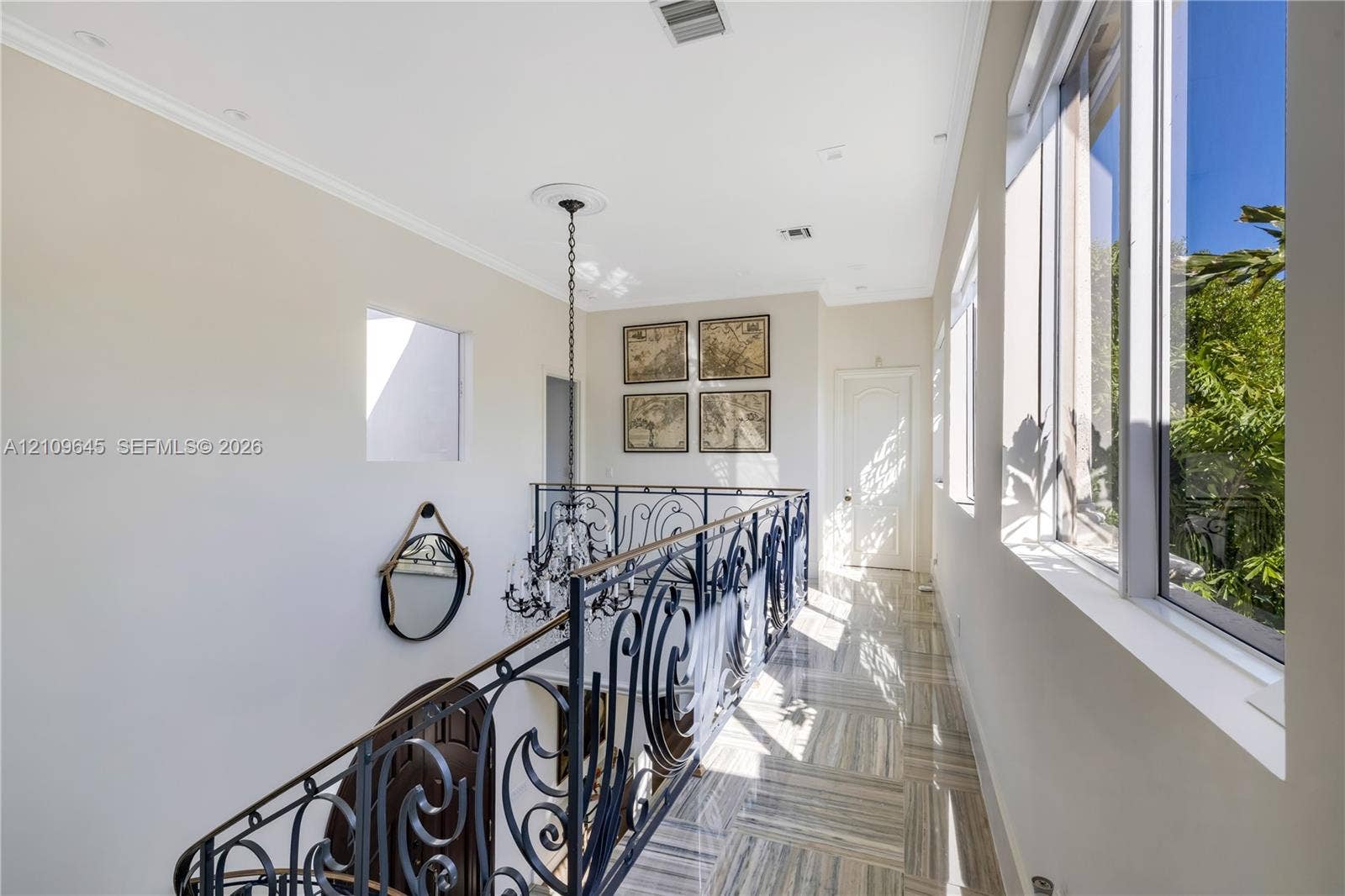 332 Costanera Road, Coral Gables, FL 33143 Hallway featuring large-format tile flooring, ornate wrought-iron railings, high ceilings with recessed lighting, and a multi-tiered crystal chandelier