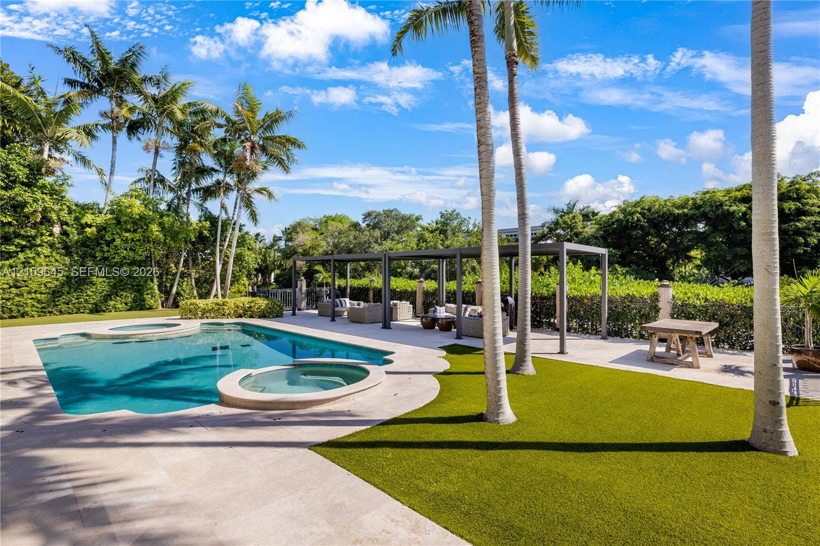 332 Costanera Road, Coral Gables, FL 33143 Backyard featuring an in-ground swimming pool, attached spa, stone-finish pool deck, synthetic turf lawn, and metal-frame pergola