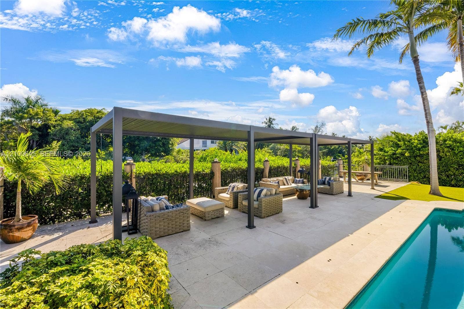 332 Costanera Road, Coral Gables, FL 33143 Outdoor living space featuring a modern metal pergola, paved stone pool deck, and inground swimming pool surrounded by mature landscape hedging
