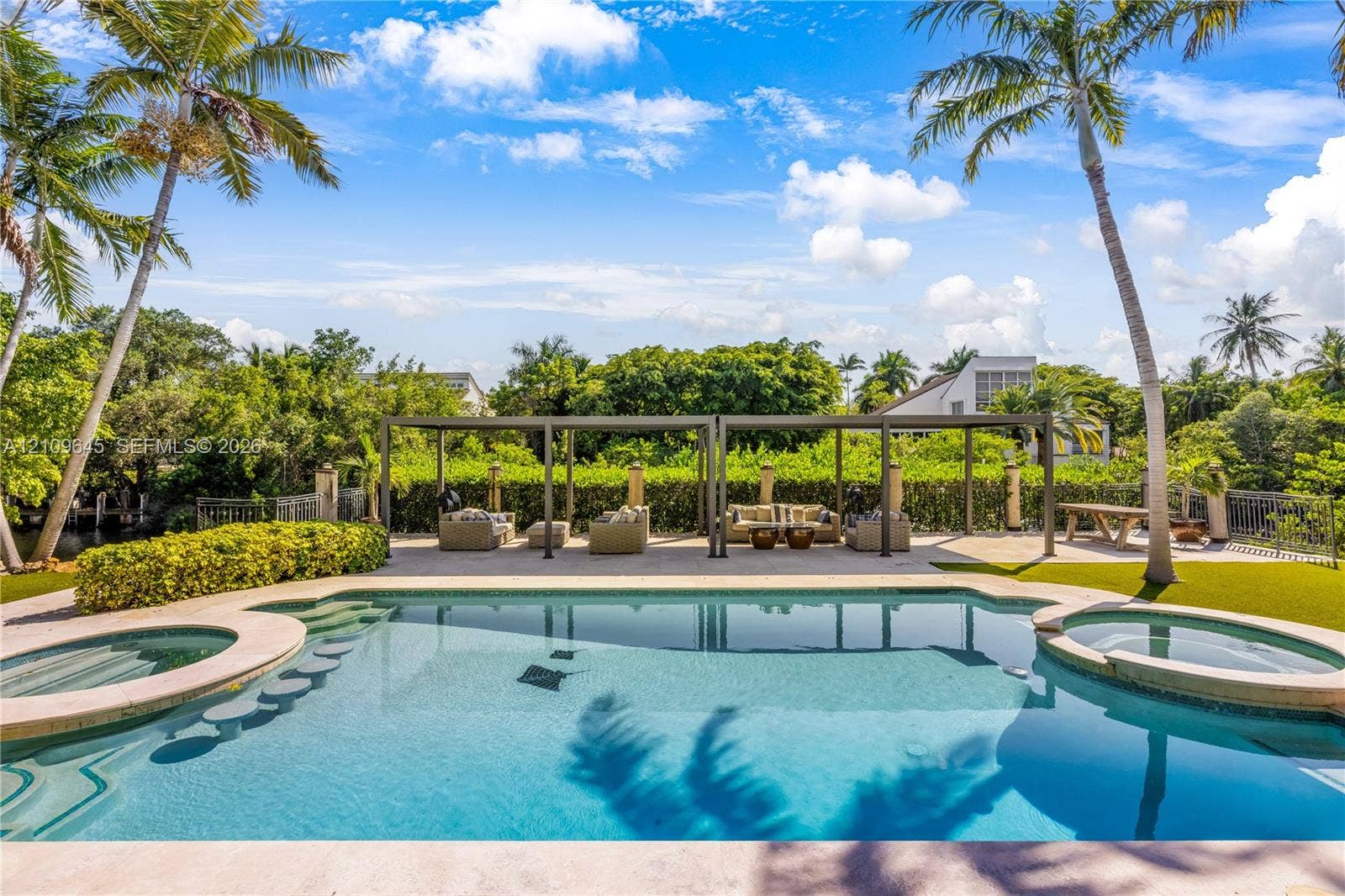 332 Costanera Road, Coral Gables, FL 33143 In-ground swimming pool with built-in wading stools and integrated spa, complemented by a stone-paved pool deck, covered pergola structure, and mature palm trees