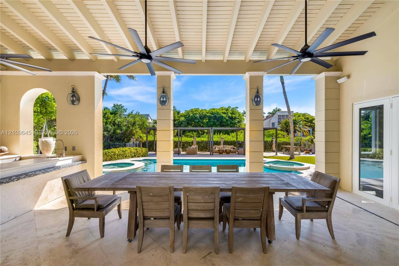 332 Costanera Road, Coral Gables, FL 33143 Covered patio featuring a beamed ceiling with dual overhead fans, stone flooring, a built-in outdoor kitchen, and pool with an integrated spa