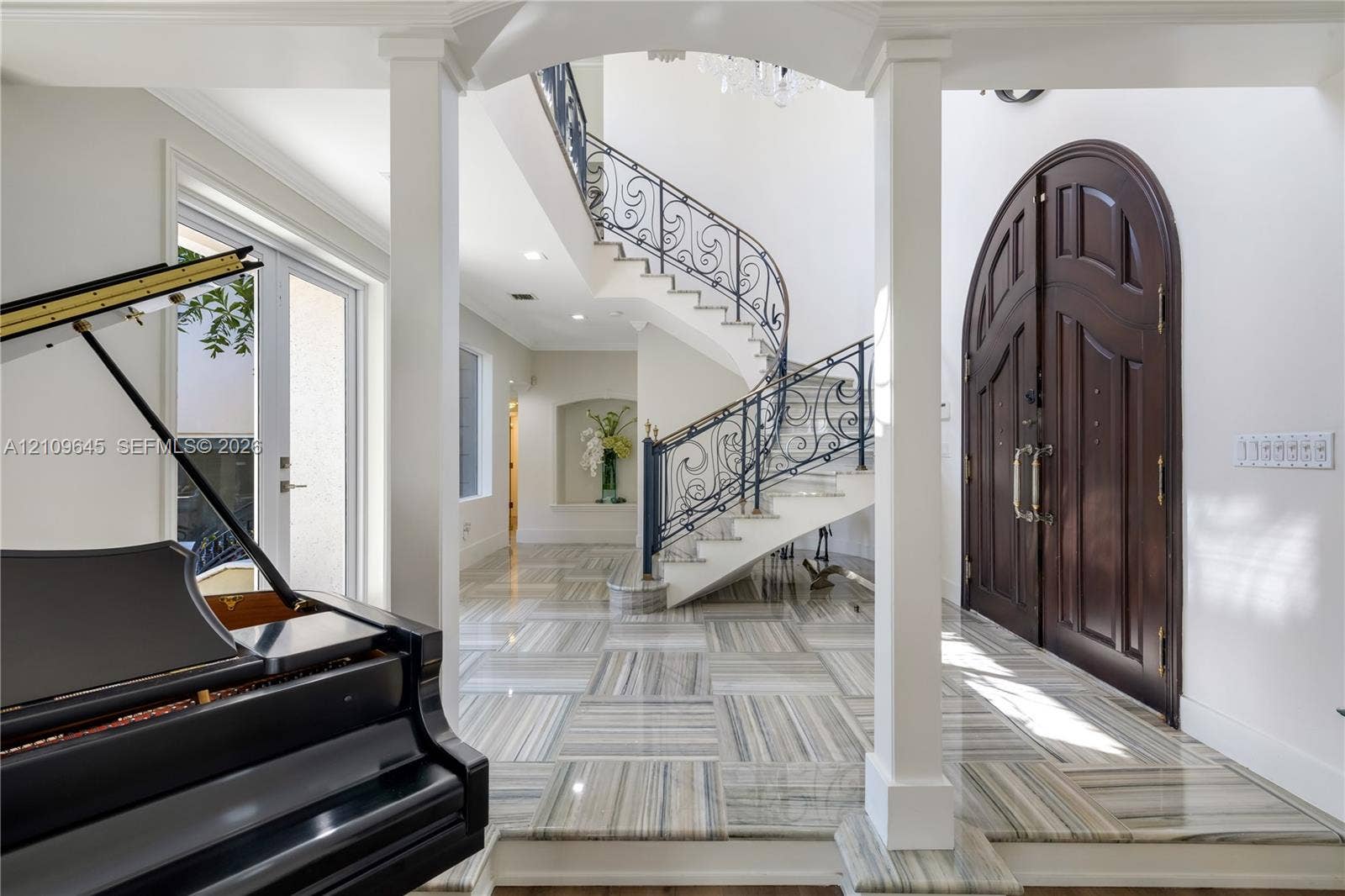 332 Costanera Road, Coral Gables, FL 33143 Foyer featuring arched double entry doors, curved staircase with ornamental metal railings, stone flooring with linear patterns, recessed lighting, and a built-in wall niche