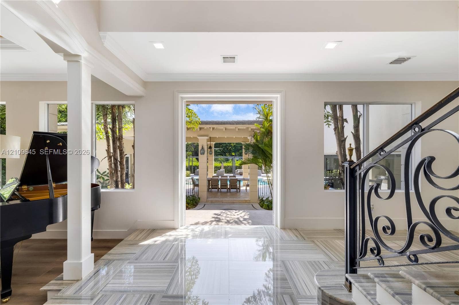 332 Costanera Road, Coral Gables, FL 33143 Foyer featuring large-format light-toned stone flooring, decorative iron stair railing, recessed ceiling lighting, and expansive square-cased entry to the outdoor patio