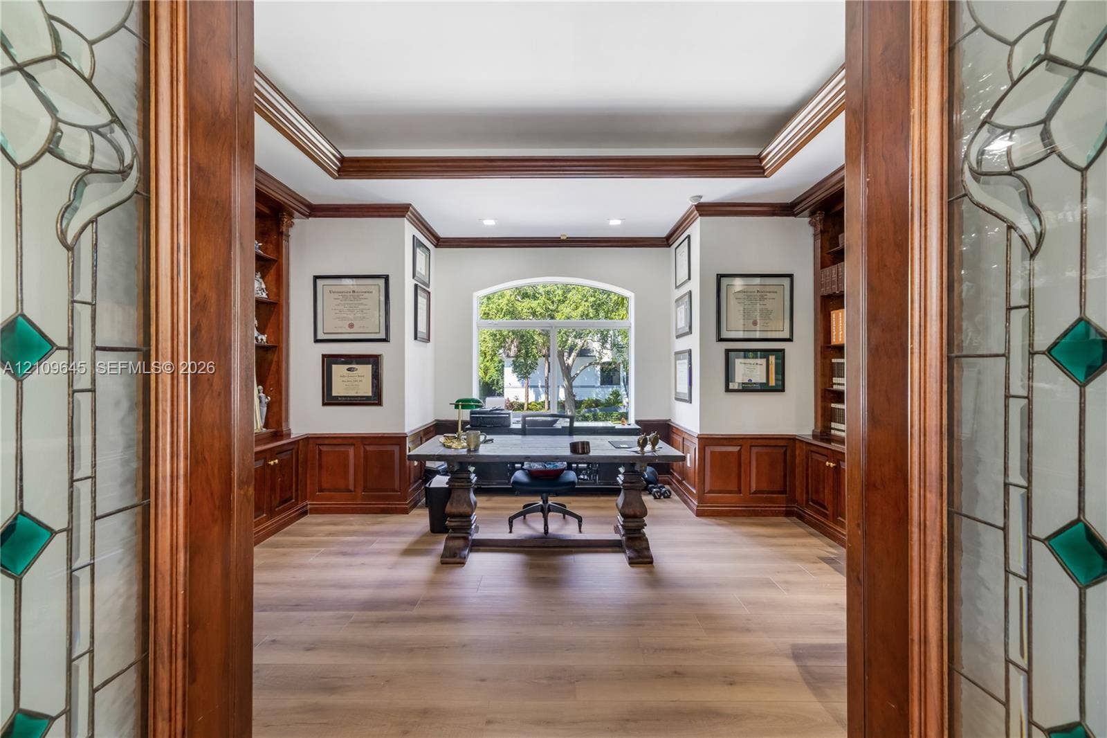 332 Costanera Road, Coral Gables, FL 33143 Custom woodwork study featuring wood-paneled wainscoting, floor-to-ceiling built-in cabinetry, arched window, recessed lighting, and glass-paneled double doors with decorative detailing