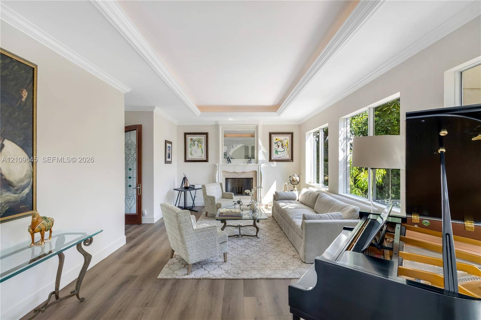 332 Costanera Road, Coral Gables, FL 33143 Living area featuring a tray ceiling, wood-finish flooring, a traditional fireplace with a decorative mantel, and multi-pane windows