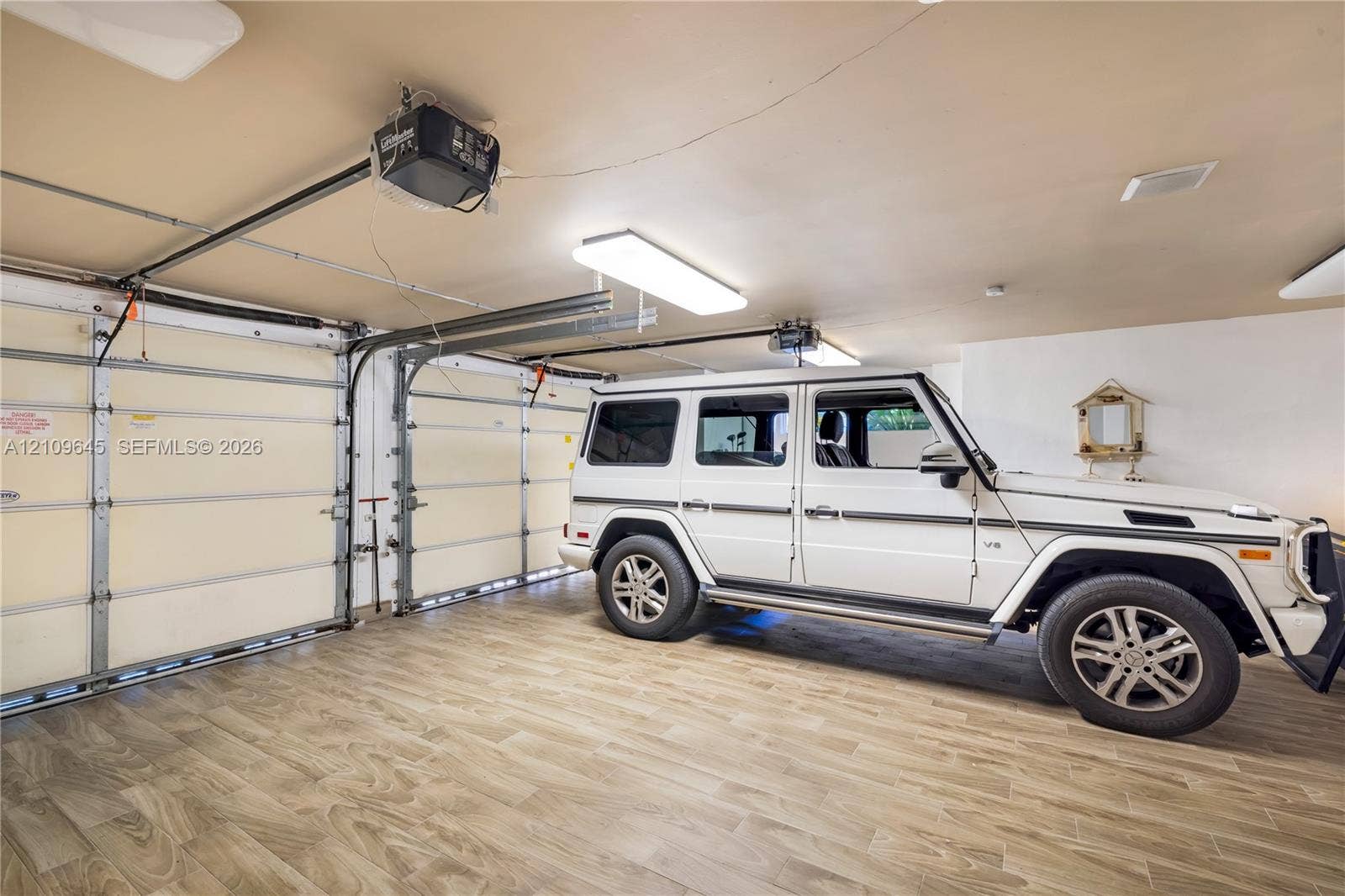 332 Costanera Road, Coral Gables, FL 33143 Garage featuring wood-finish flooring, dual motorized garage door openers, and rectangular LED light fixtures