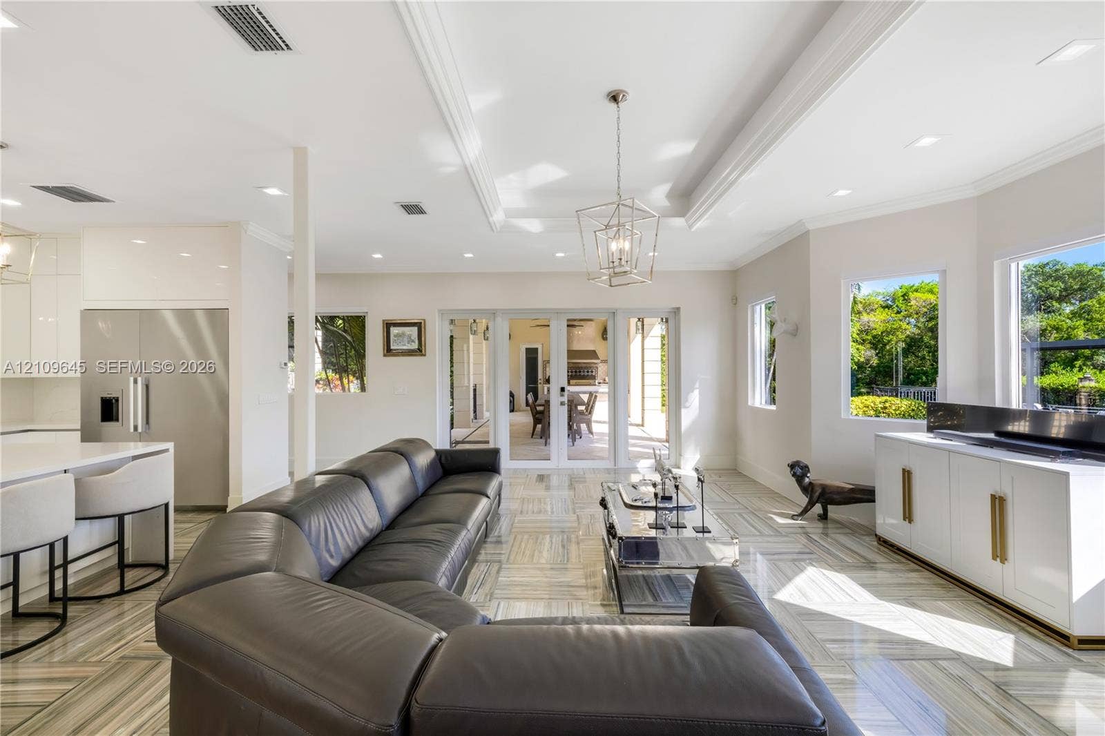 332 Costanera Road, Coral Gables, FL 33143 Open-concept living space featuring high ceilings with crown molding, recessed lighting, geometric metal pendant fixture, large-format tile flooring, and glass-paned doors