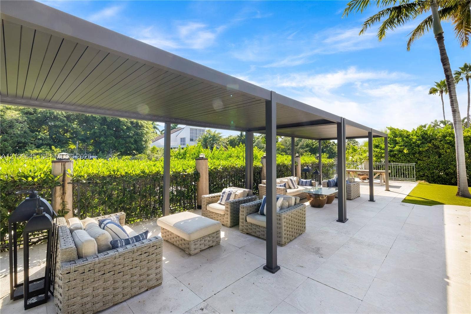 332 Costanera Road, Coral Gables, FL 33143 Covered patio featuring a structured metal pergola, large-format stone pavers, and a perimeter of mature privacy hedging