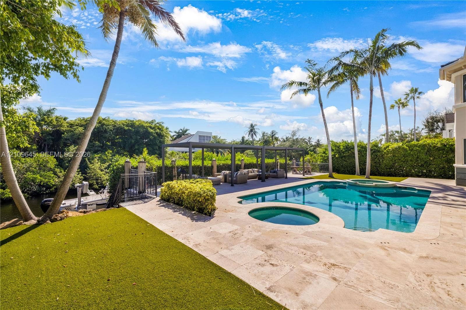332 Costanera Road, Coral Gables, FL 33143 Rear yard featuring a pool with an integrated spa, stone-finish decking, a metal pergola, and synthetic turf lawn