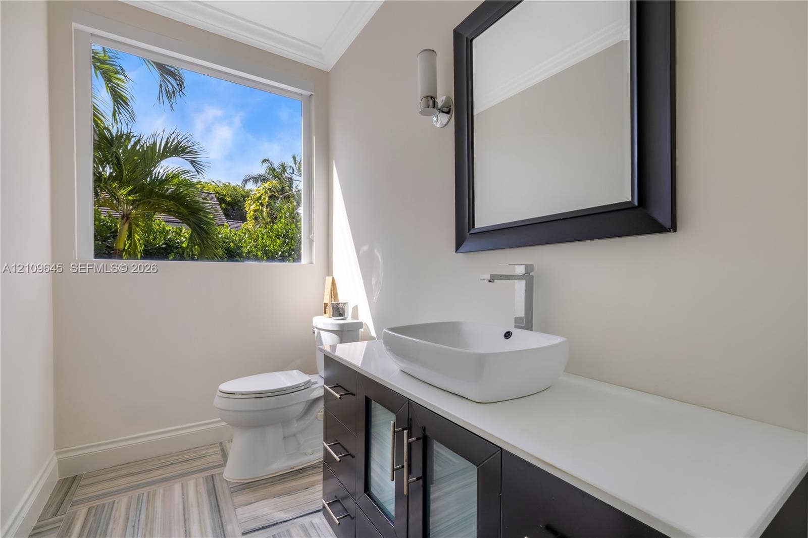 332 Costanera Road, Coral Gables, FL 33143 Modern vanity featuring a stone countertop, vessel sink, and metallic hardware, complemented by patterned tile flooring and a wall-mounted light fixture