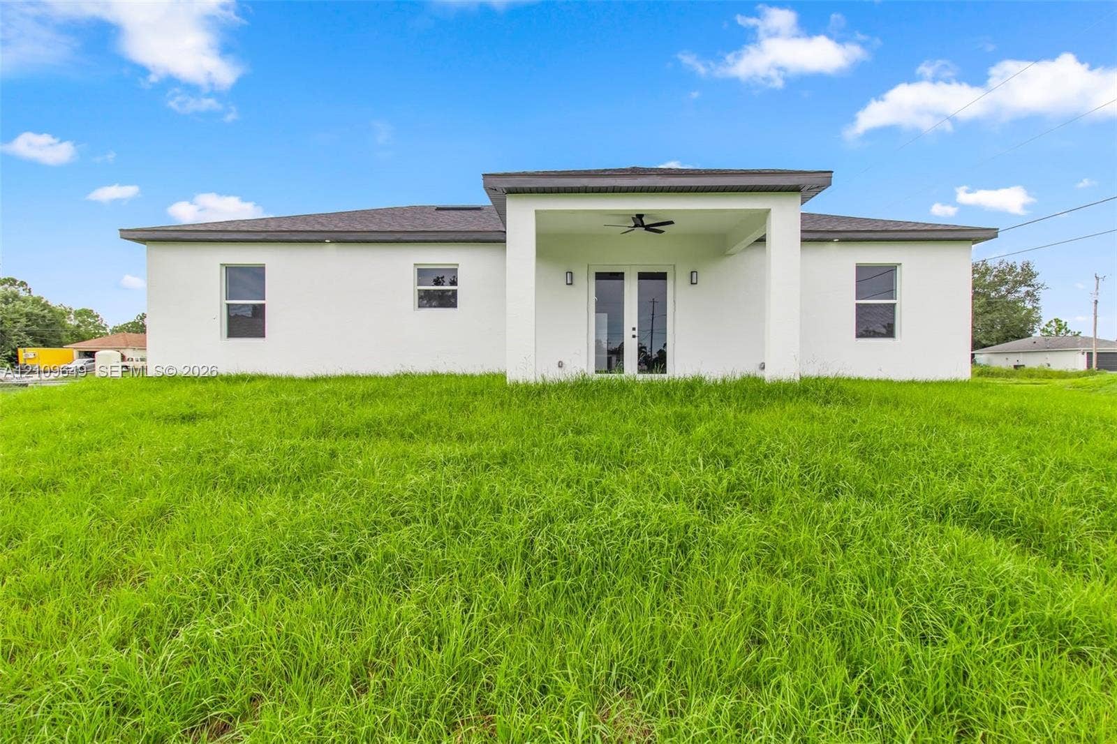 2818 42nd St Sw Lehigh Acres, Lehigh Acres, FL 33976 Single-story exterior featuring white stucco siding, a covered patio with a ceiling fan, and double glass-panel doors