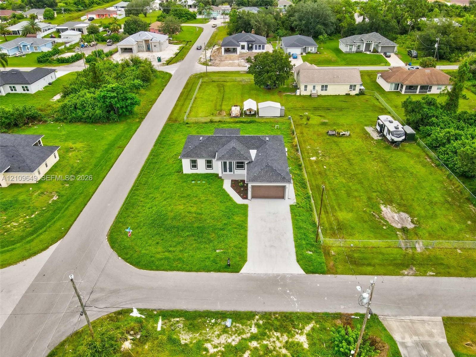 2818 42nd St Sw Lehigh Acres, Lehigh Acres, FL 33976 Single-story residence featuring a dark shingled roof, attached two-car garage, concrete driveway, and expansive corner lot