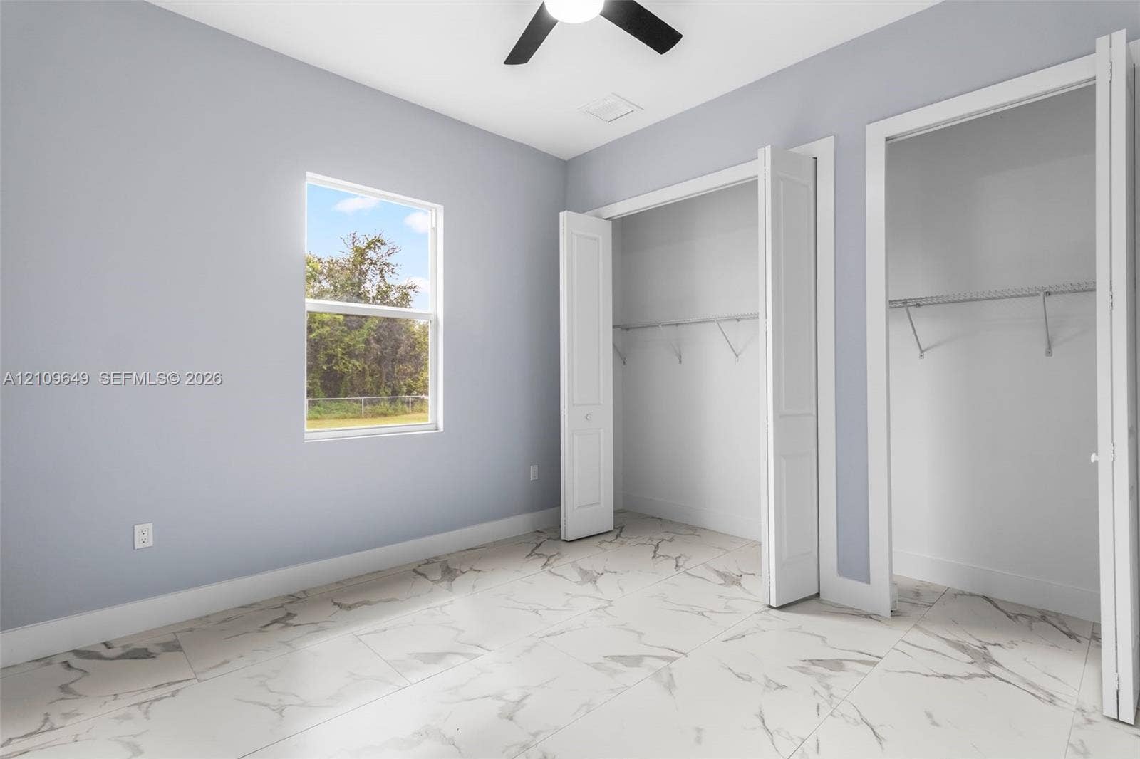 2818 42nd St Sw Lehigh Acres, Lehigh Acres, FL 33976 Room featuring large-format tile flooring with a neutral veining pattern, dual closets with bi-fold doors, a single-hung window, and a ceiling fan