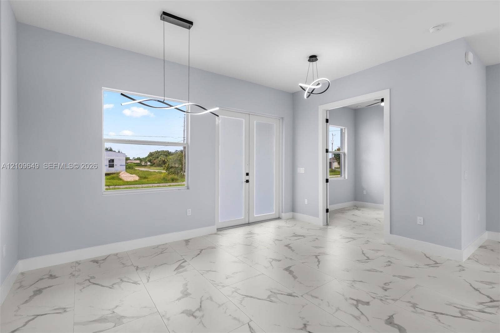 2818 42nd St Sw Lehigh Acres, Lehigh Acres, FL 33976 Large-format stone-finish flooring with veining detail, double-entry glass paneled doors, and contemporary sculptural overhead lighting fixtures