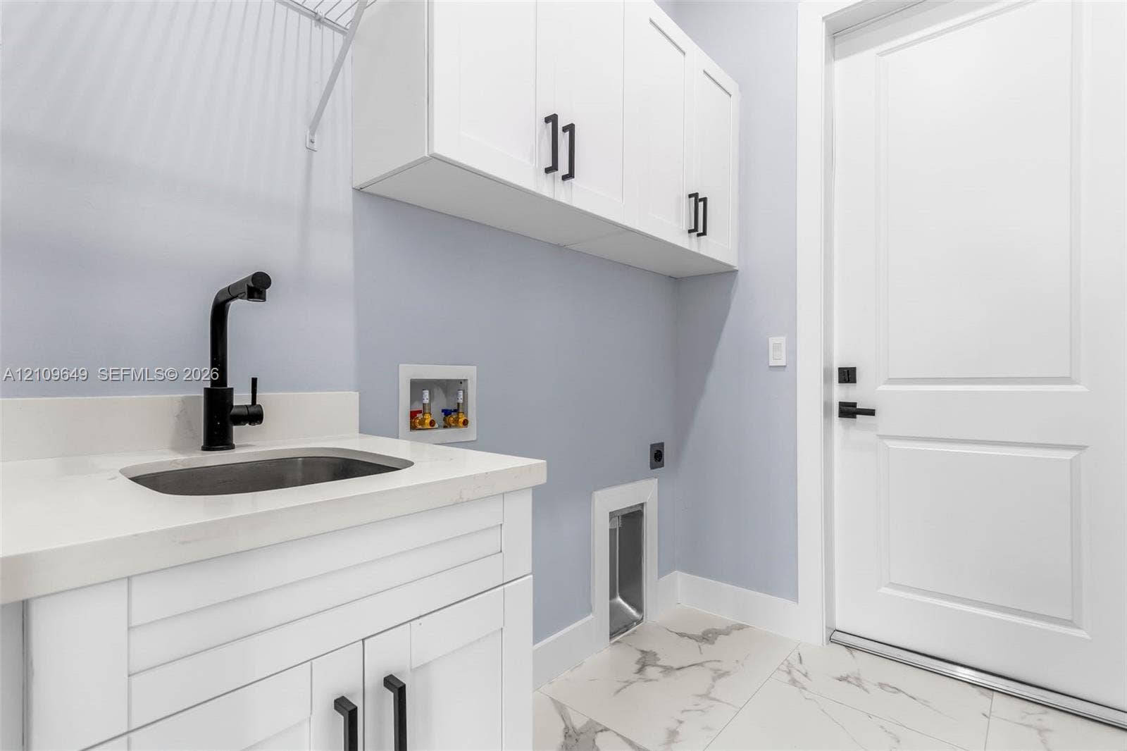2818 42nd St Sw Lehigh Acres, Lehigh Acres, FL 33976 Utility area featuring shaker-style white cabinetry, stone-finish countertops, an undermount sink with a matte black faucet, and large-format tile flooring