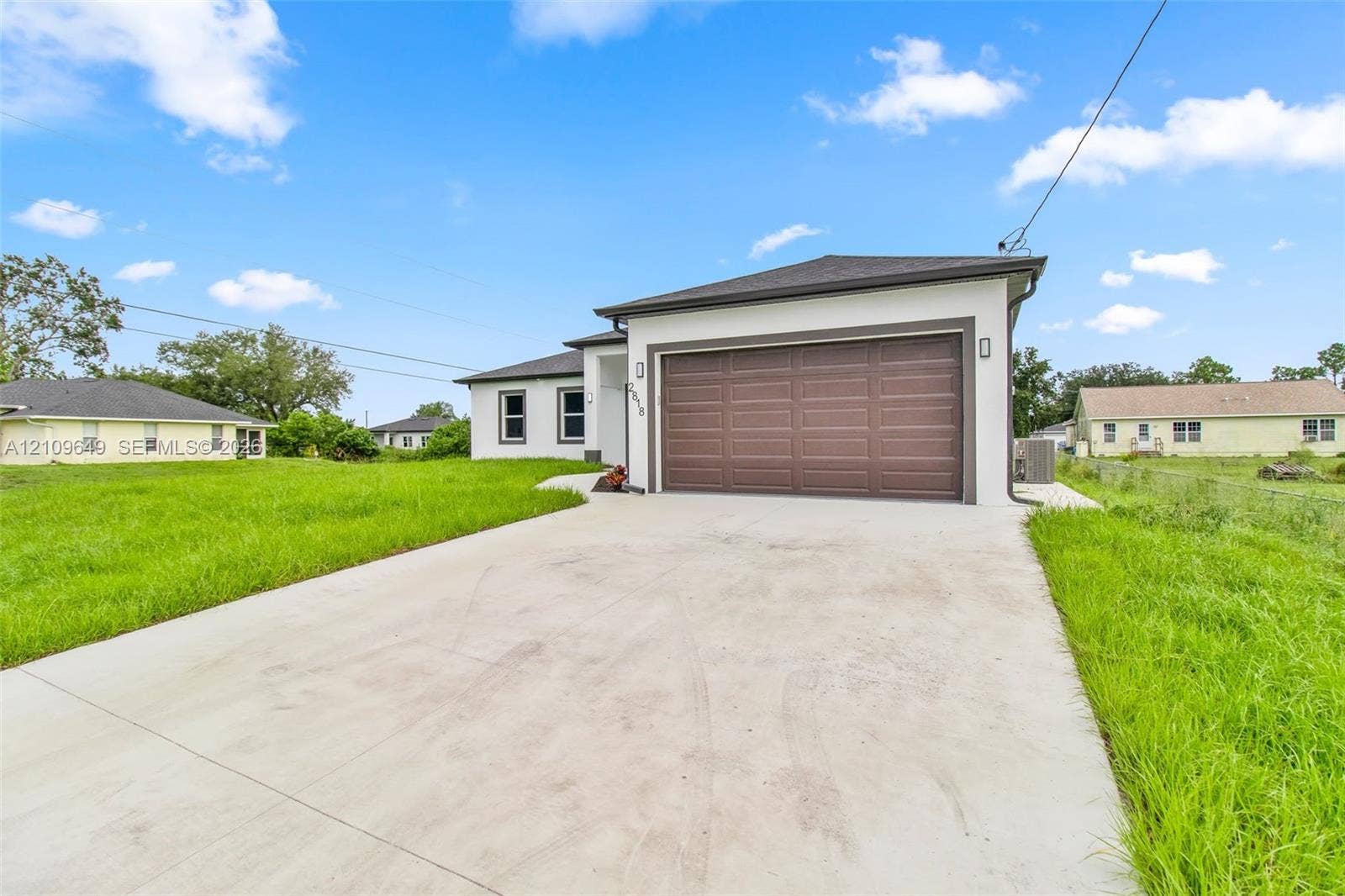 2818 42nd St Sw Lehigh Acres, Lehigh Acres, FL 33976 Single-story exterior featuring a stucco facade, concrete driveway, and attached two-car garage with a paneled door