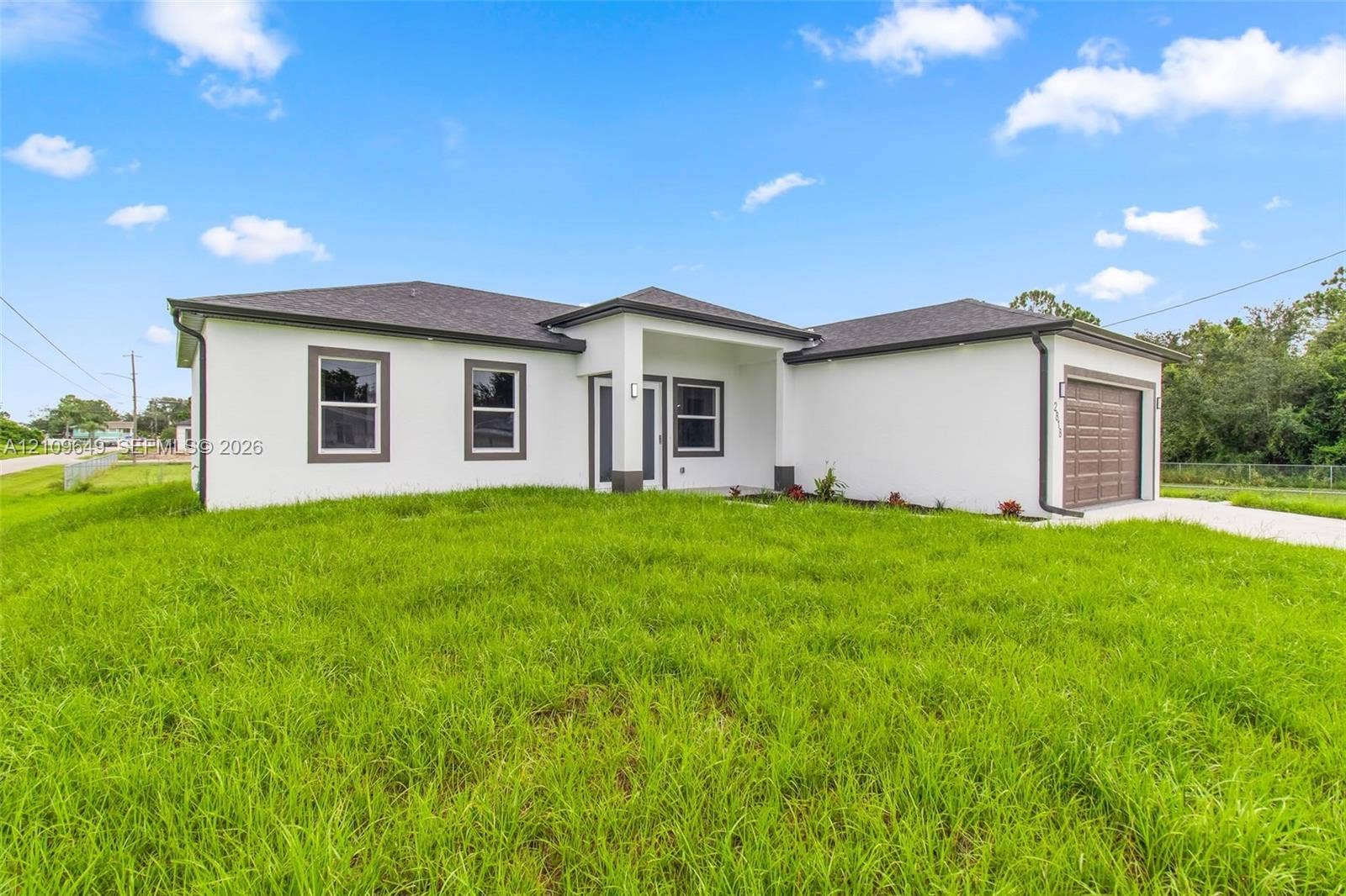 2818 42nd St Sw Lehigh Acres, Lehigh Acres, FL 33976 Single-story exterior featuring white stucco siding, a covered entryway, a dark-toned asphalt shingle roof, and an attached two-car garage