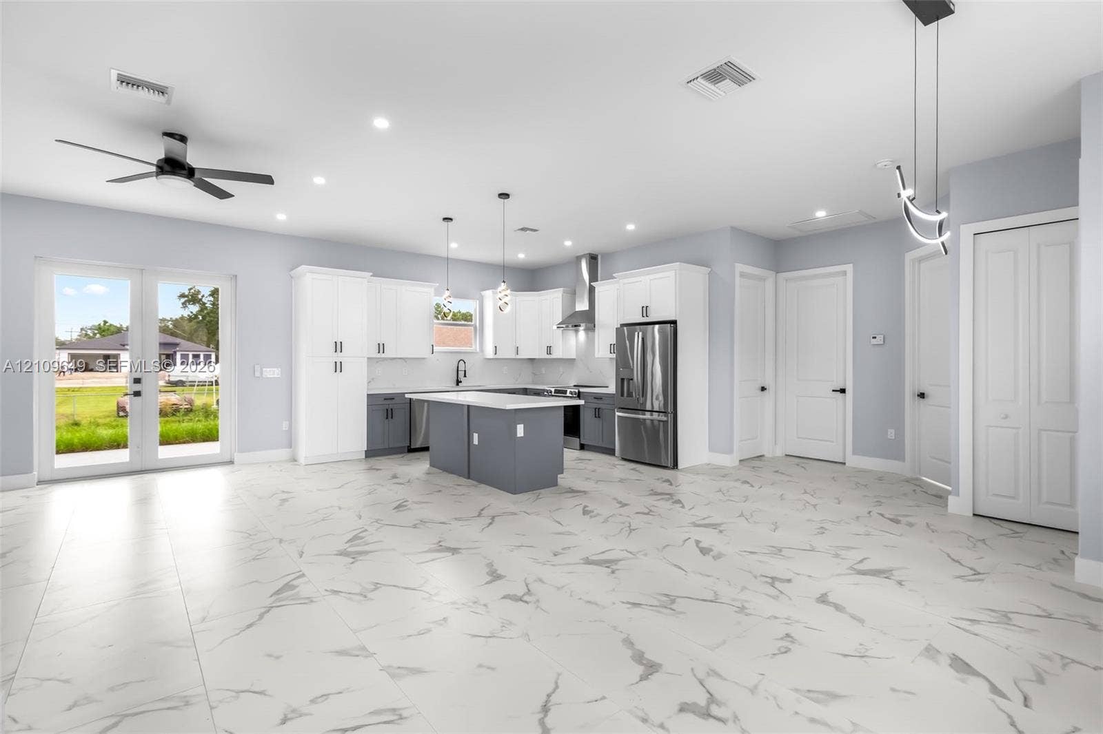2818 42nd St Sw Lehigh Acres, Lehigh Acres, FL 33976 Open-concept kitchen featuring two-toned cabinetry, a central island with a stone-finish countertop, stainless steel appliances, porcelain tile flooring, and glass-paneled double doors