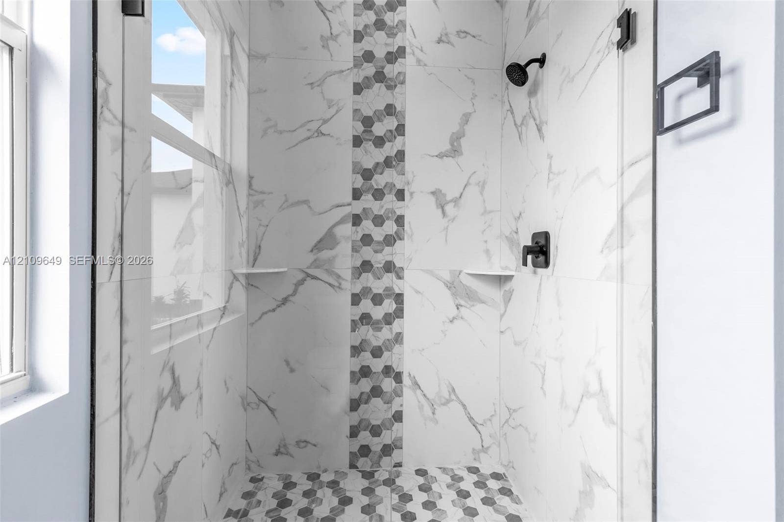 2818 42nd St Sw Lehigh Acres, Lehigh Acres, FL 33976 Walk-in shower featuring large-format stone-patterned wall tiles, a vertical decorative hexagonal tile inlay, a matching hexagonal tile floor, a glass enclosure, and matte black fixtures