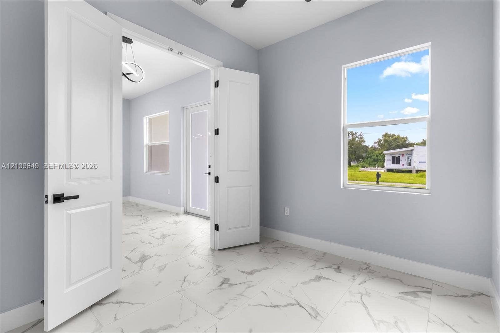 2818 42nd St Sw Lehigh Acres, Lehigh Acres, FL 33976 Large-format white tile flooring with grey veining, crisp neutral wall paint, multi-panel double doors with matte black hardware, and double-pane window