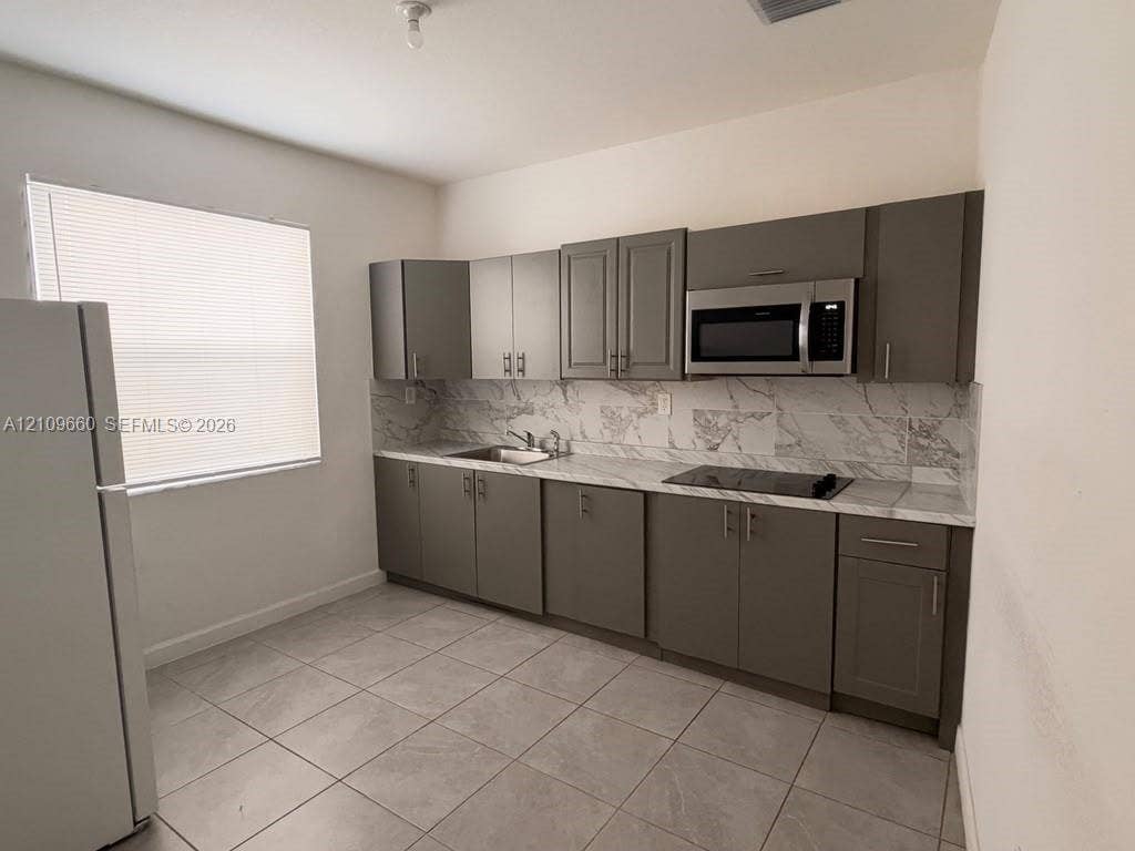 23275 SW 133 Rd Avenue, #2, Homestead, Homestead, FL 33032 Kitchen featuring gray shaker-style cabinetry, stone-patterned backsplash, light-toned countertop, built-in microwave, and tile flooring