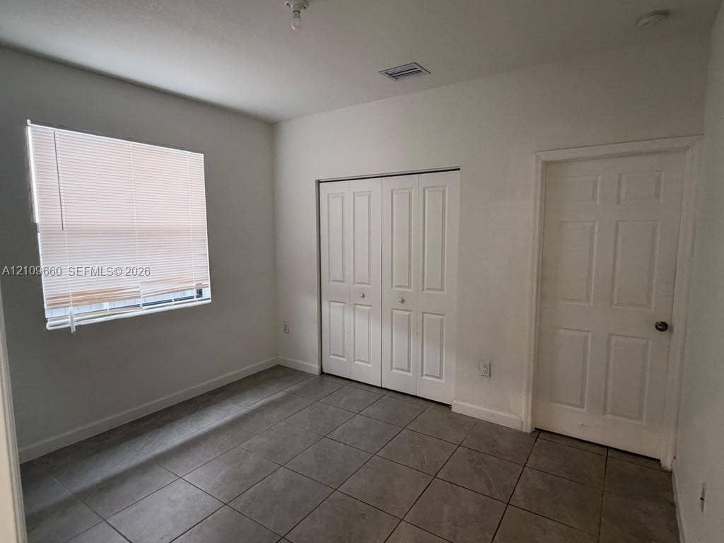 23275 SW 133 Rd Avenue, #2, Homestead, Homestead, FL 33032 Room featuring neutral-toned floor tiling, a multi-panel door, built-in closet with double doors, and a window with horizontal blinds