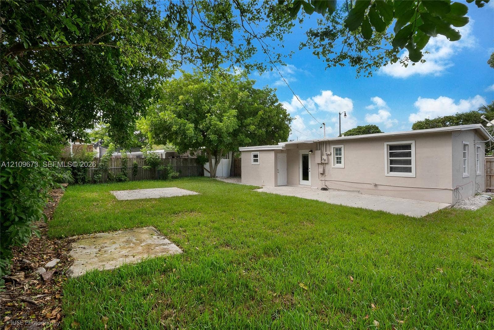 1748 NE 49th Street, Pompano Beach, FL 33064 Backyard featuring a grass lawn, concrete patio, perimeter wood fencing, and mature trees