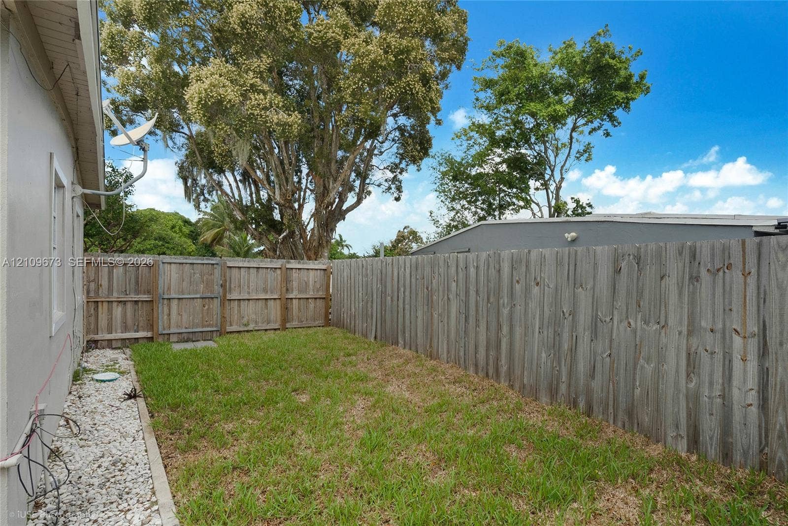 1748 NE 49th Street, Pompano Beach, FL 33064 Rear exterior space featuring a grass lawn, white stone border, wood-finish privacy fencing, and a gated access point