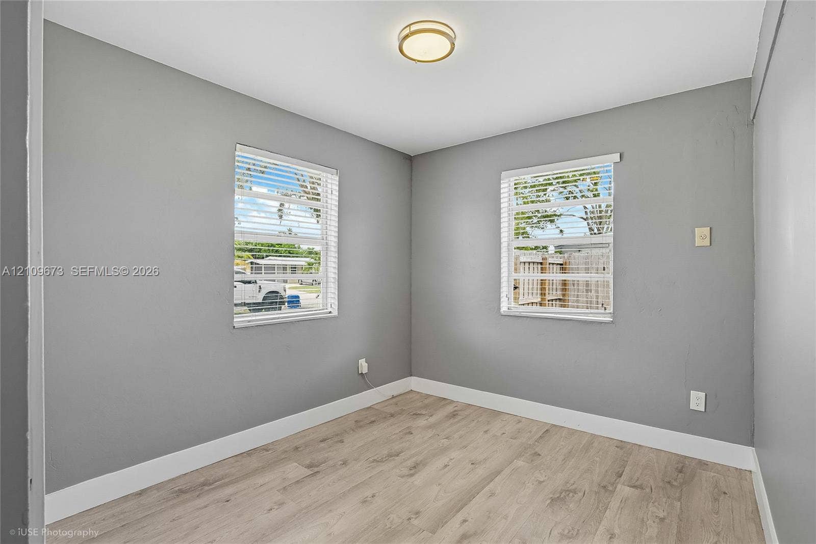 1748 NE 49th Street, Pompano Beach, FL 33064 Neutral-toned interior featuring wood-finish flooring, dual windows with blinds, and a flush-mount circular ceiling light fixture