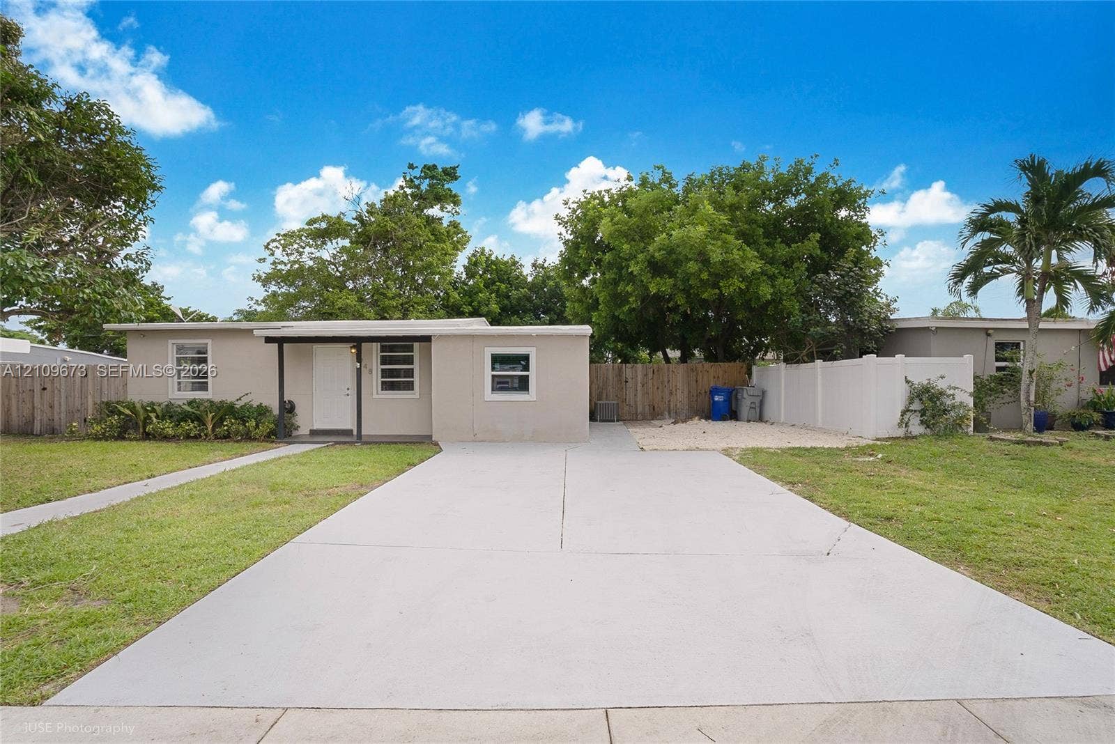 1748 NE 49th Street, Pompano Beach, FL 33064 Single-story exterior featuring a concrete driveway, covered front entryway, horizontal sliding windows, and perimeter privacy fencing