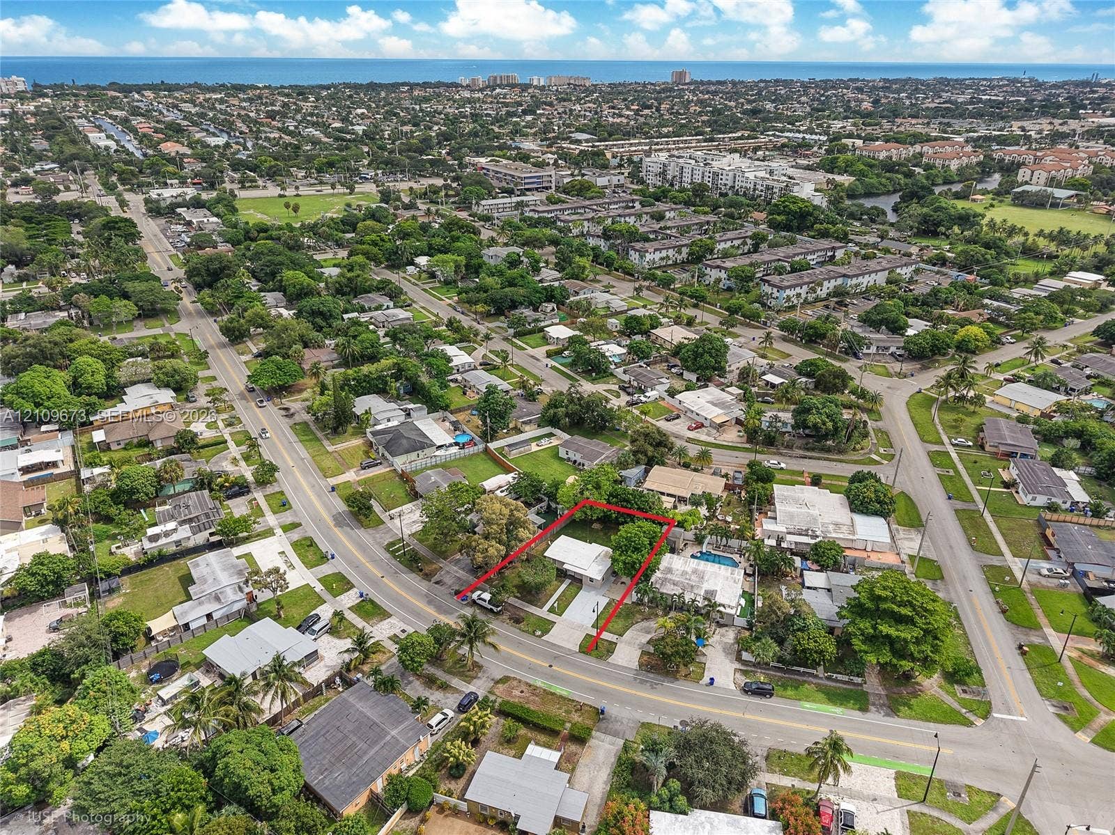 1748 NE 49th Street, Pompano Beach, FL 33064 Aerial perspective of a residential lot featuring a detached structure, concrete driveway, mature canopy trees, and established landscaping