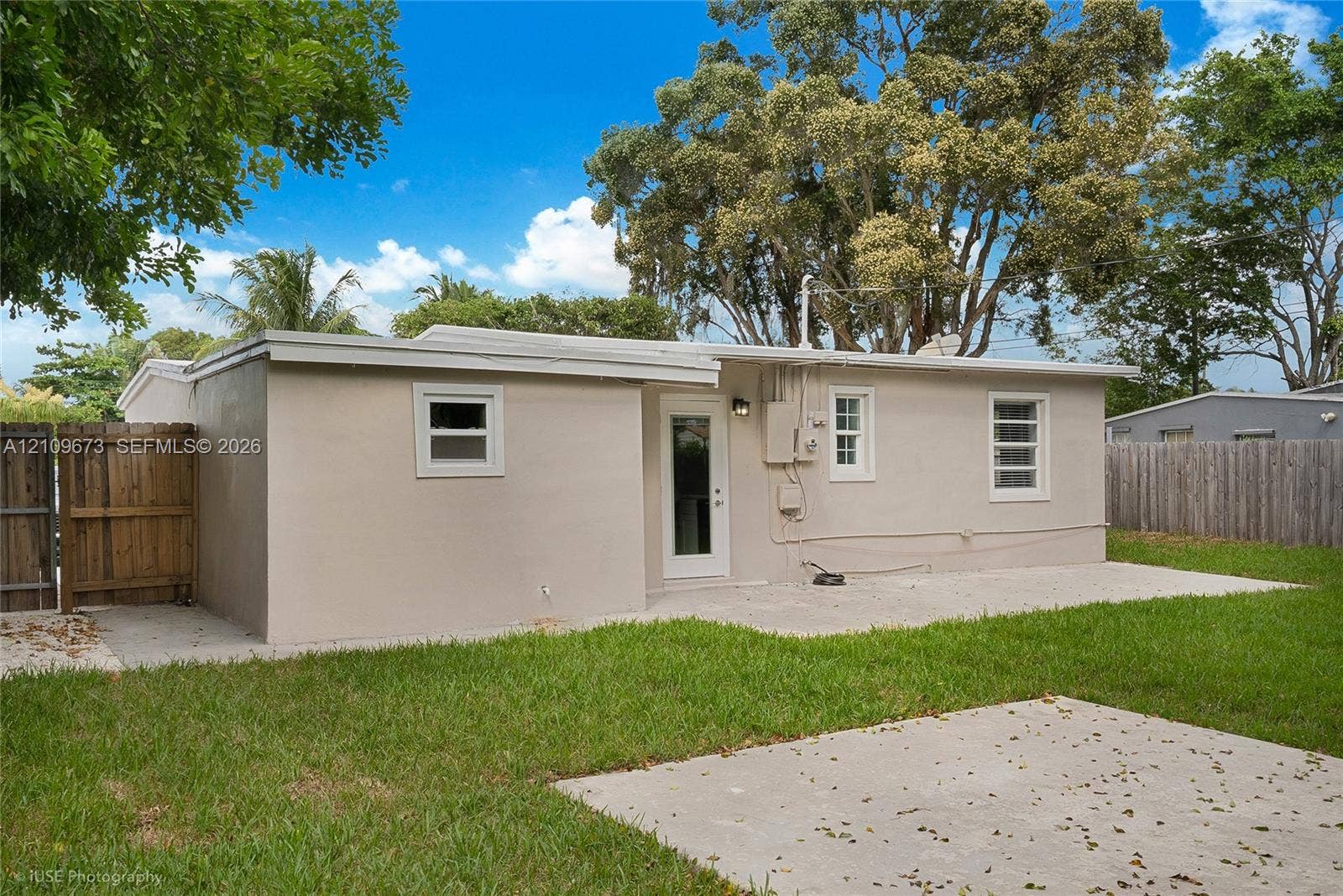 1748 NE 49th Street, Pompano Beach, FL 33064 Exterior rear elevation featuring a concrete patio, stucco siding, multi-lite windows, and a wood privacy fence