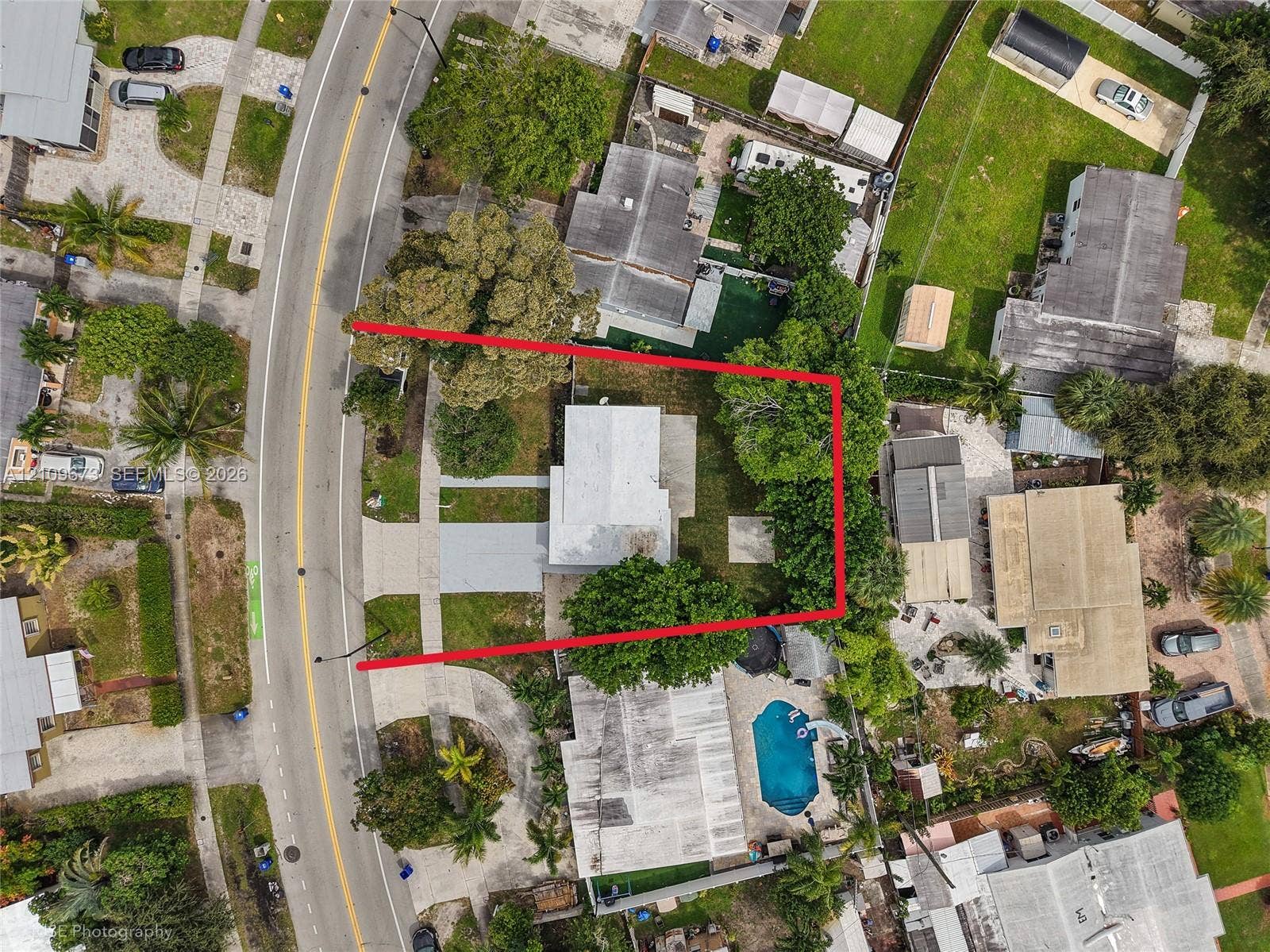 1748 NE 49th Street, Pompano Beach, FL 33064 Aerial perspective featuring a rectangular parcel with a paved driveway, concrete walkways, and mature trees