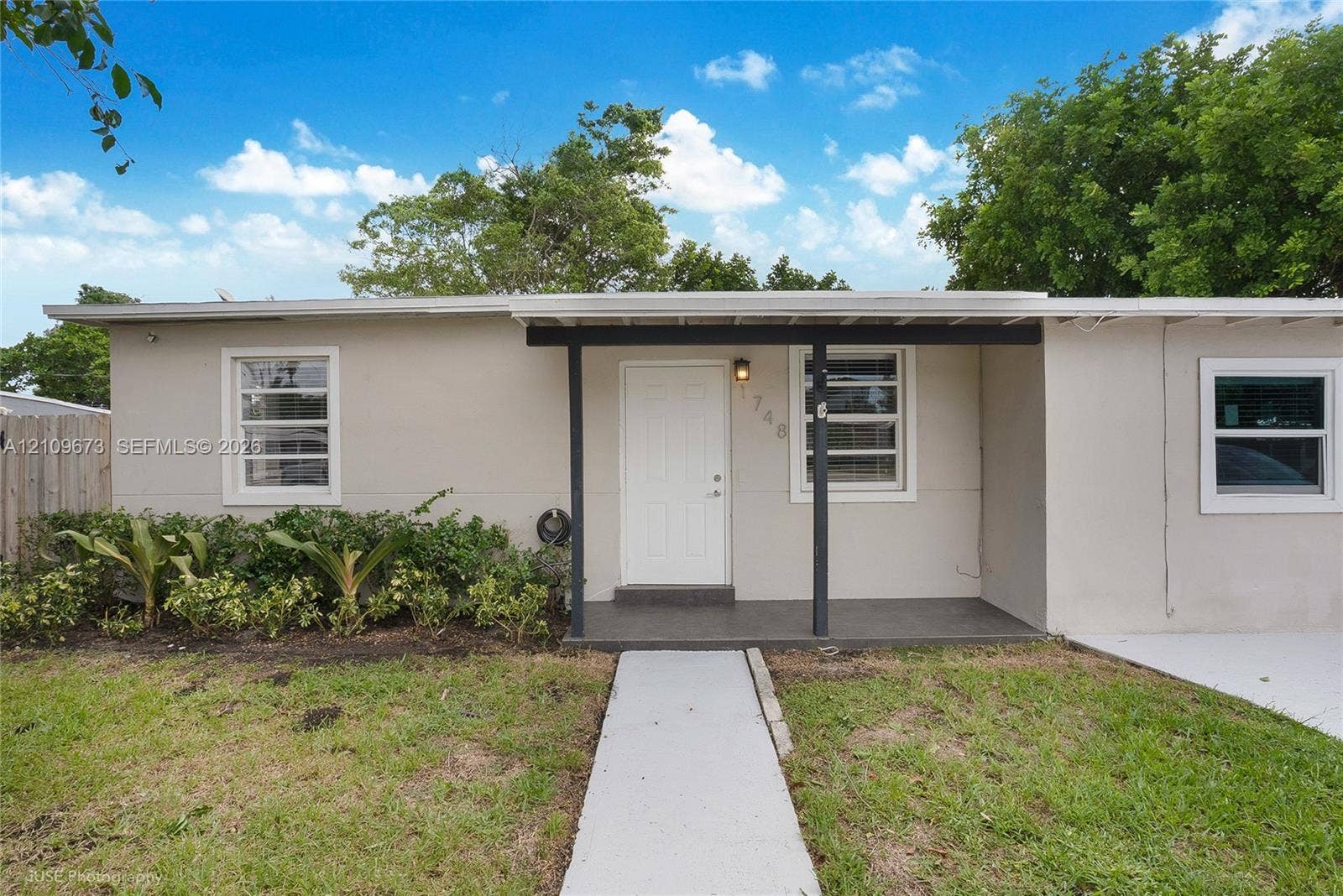 1748 NE 49th Street, Pompano Beach, FL 33064 Single-story exterior featuring a neutral-toned facade, covered front entryway, concrete walkway, and landscaped garden beds