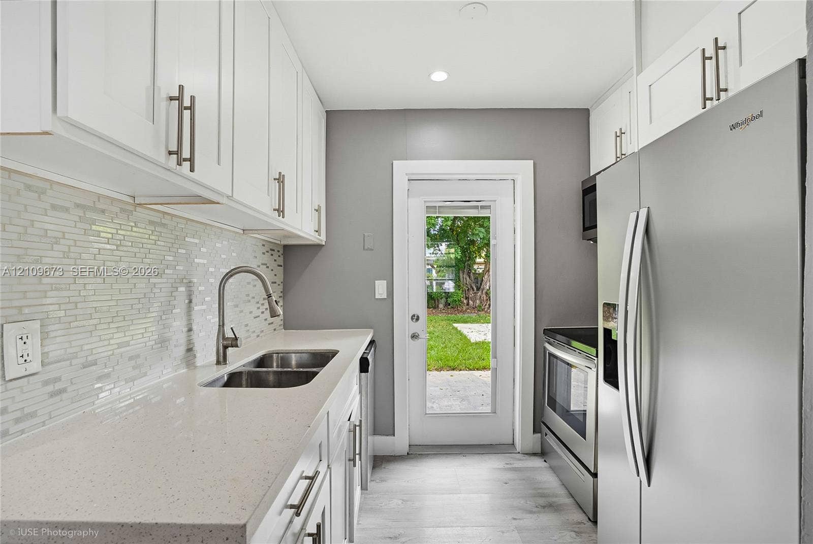 1748 NE 49th Street, Pompano Beach, FL 33064 Kitchen featuring white shaker-style cabinetry, solid-surface countertops, a mosaic tile backsplash, stainless steel appliances, and wood-finish flooring