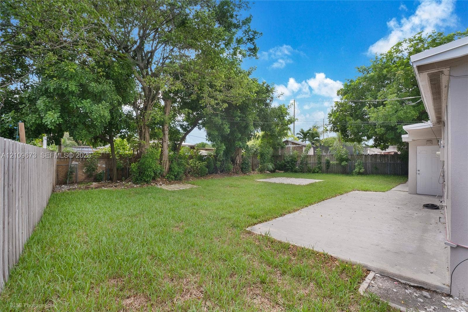 1748 NE 49th Street, Pompano Beach, FL 33064 Spacious backyard featuring a concrete patio, perimeter wood fencing, and mature trees