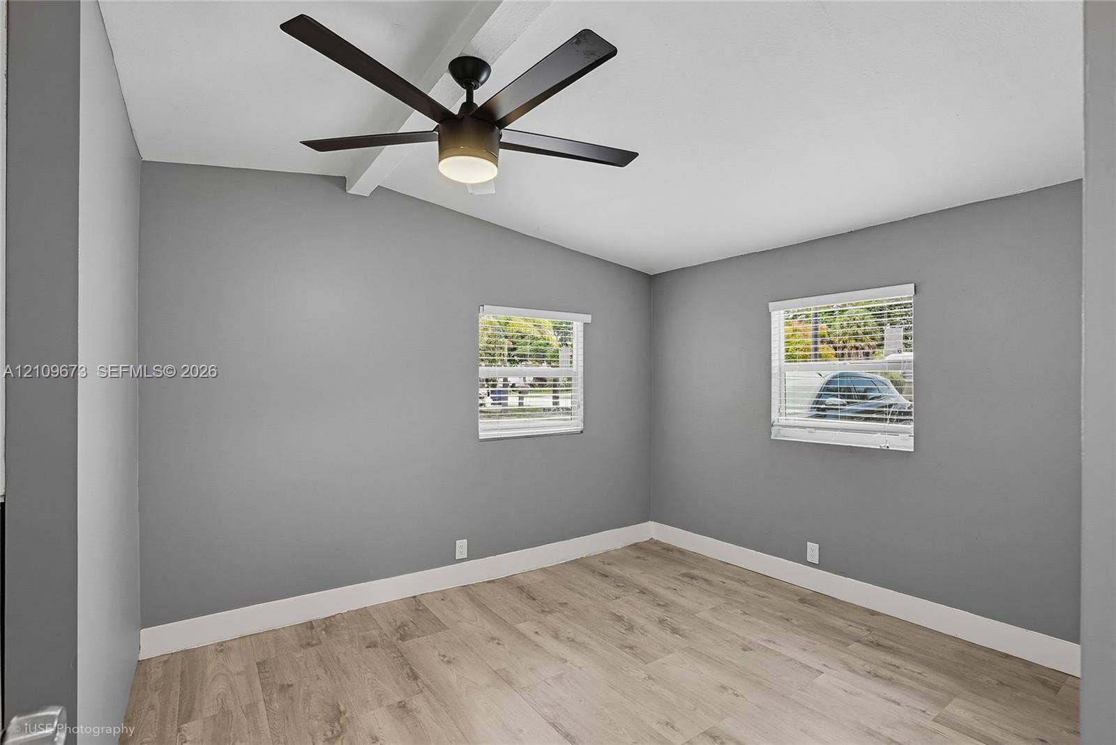 1748 NE 49th Street, Pompano Beach, FL 33064 Room featuring wood-finish flooring, vaulted ceilings with an exposed beam, a matte black ceiling fan with integrated lighting, and dual windows with horizontal blinds