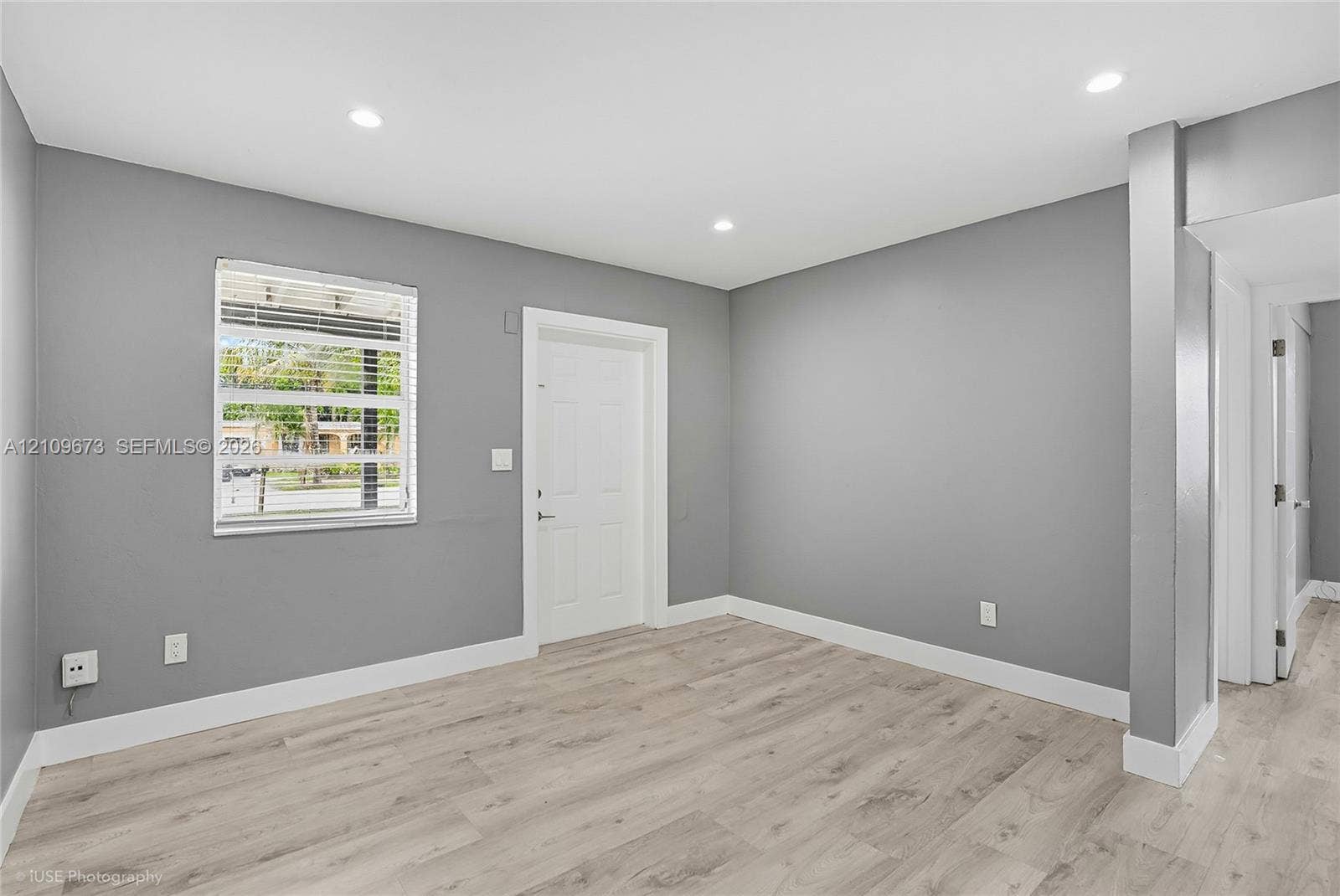 1748 NE 49th Street, Pompano Beach, FL 33064 Neutral gray wall paint, light-toned wood-finish flooring, recessed ceiling lighting, and a window with horizontal blinds