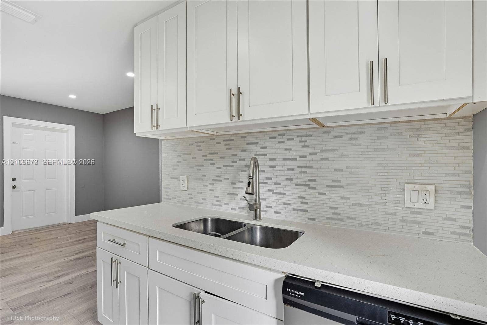 1748 NE 49th Street, Pompano Beach, FL 33064 White shaker-style cabinetry, solid surface countertop, stainless steel undermount double-basin sink with gooseneck faucet, horizontal tile backsplash, and wood-finish flooring