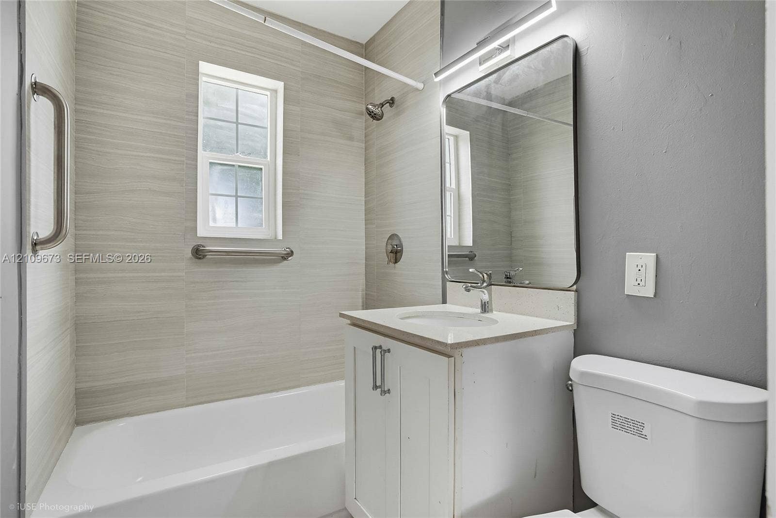1748 NE 49th Street, Pompano Beach, FL 33064 Bathroom featuring a tub-shower combination with horizontal tile surround, white vanity with an integrated countertop, wall-mounted rectangular mirror, and chrome finish fixtures