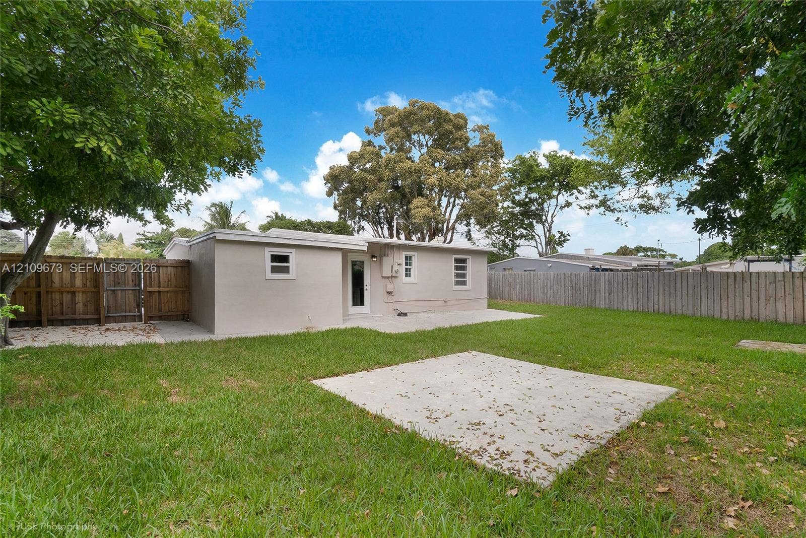 1748 NE 49th Street, Pompano Beach, FL 33064 Rear exterior featuring a concrete patio, grassy yard, and wood privacy fencing