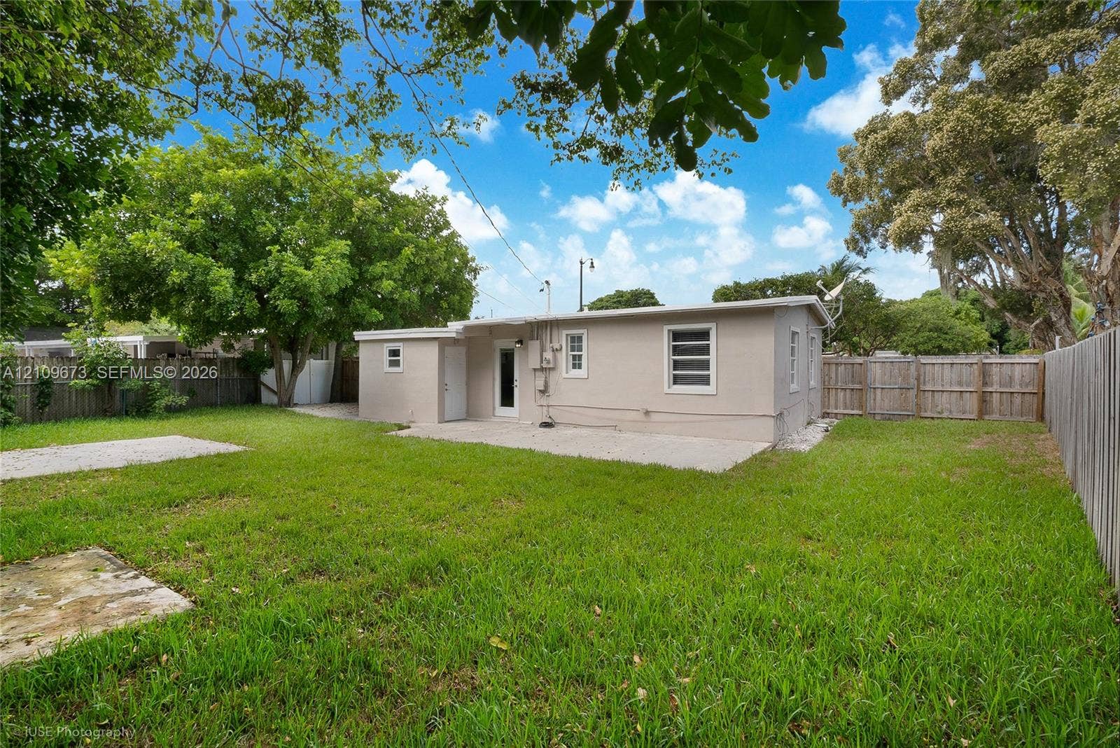 1748 NE 49th Street, Pompano Beach, FL 33064 Expansive backyard featuring a concrete patio, perimeter wood fencing, and mature trees