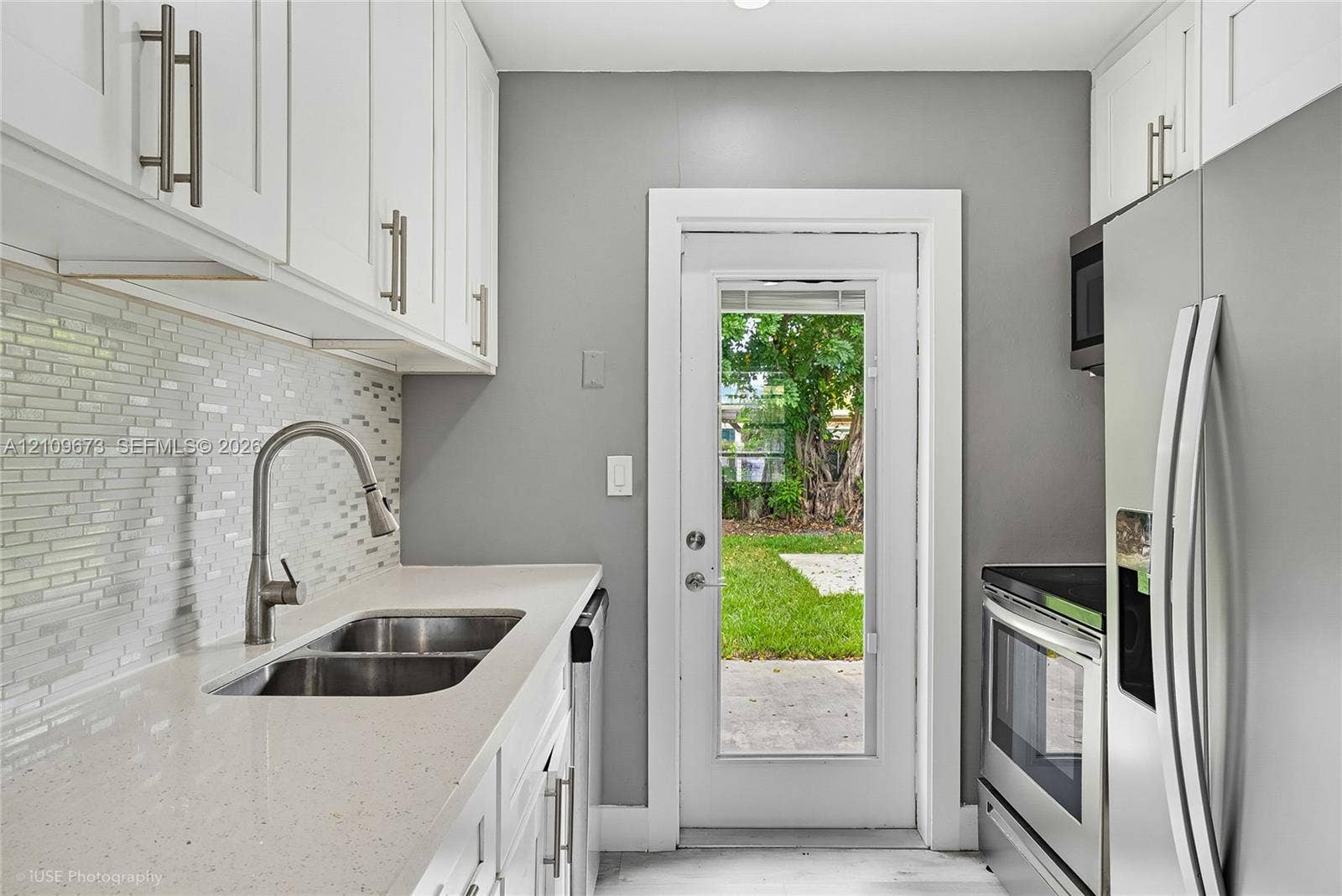 1748 NE 49th Street, Pompano Beach, FL 33064 Kitchen featuring white cabinetry, solid-surface countertops, mosaic tile backsplash, stainless steel appliances, and a glass-panel exterior door