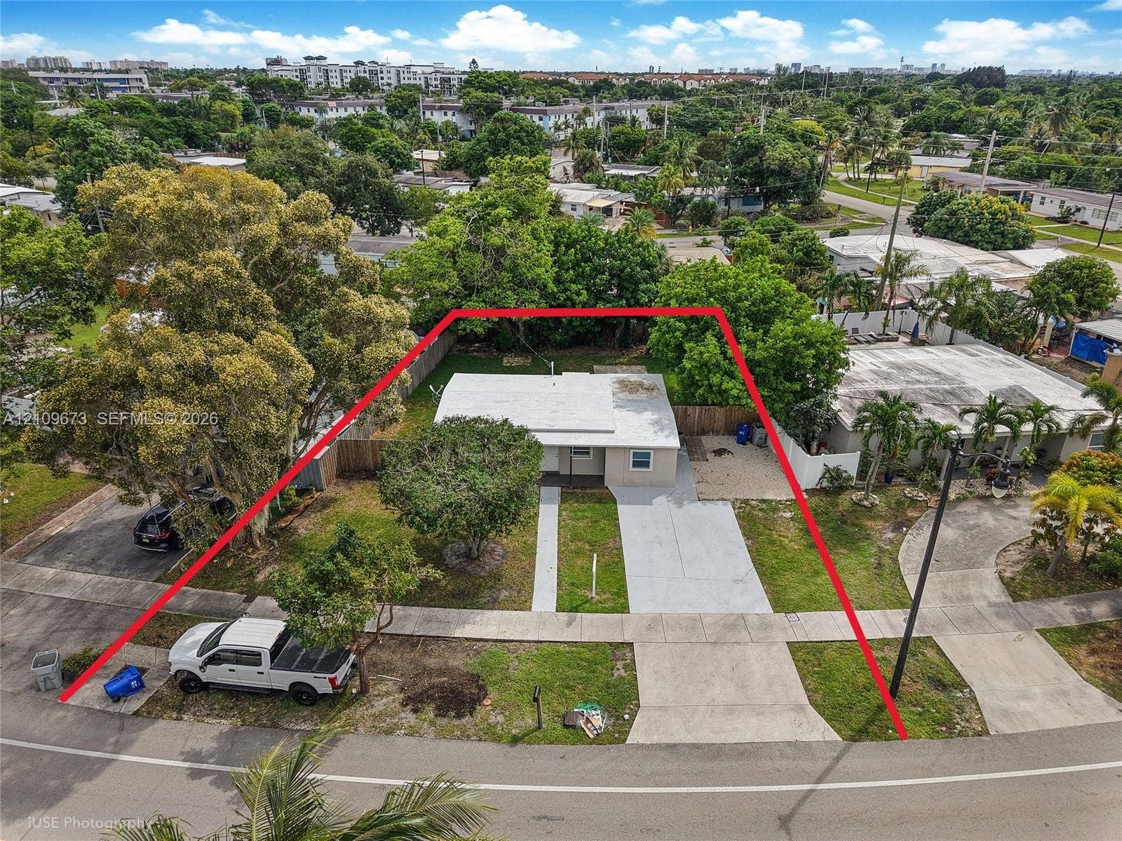 1748 NE 49th Street, Pompano Beach, FL 33064 Single-story residence featuring a flat roof, concrete driveway, fenced perimeter, and established tree canopy on a rectangular lot