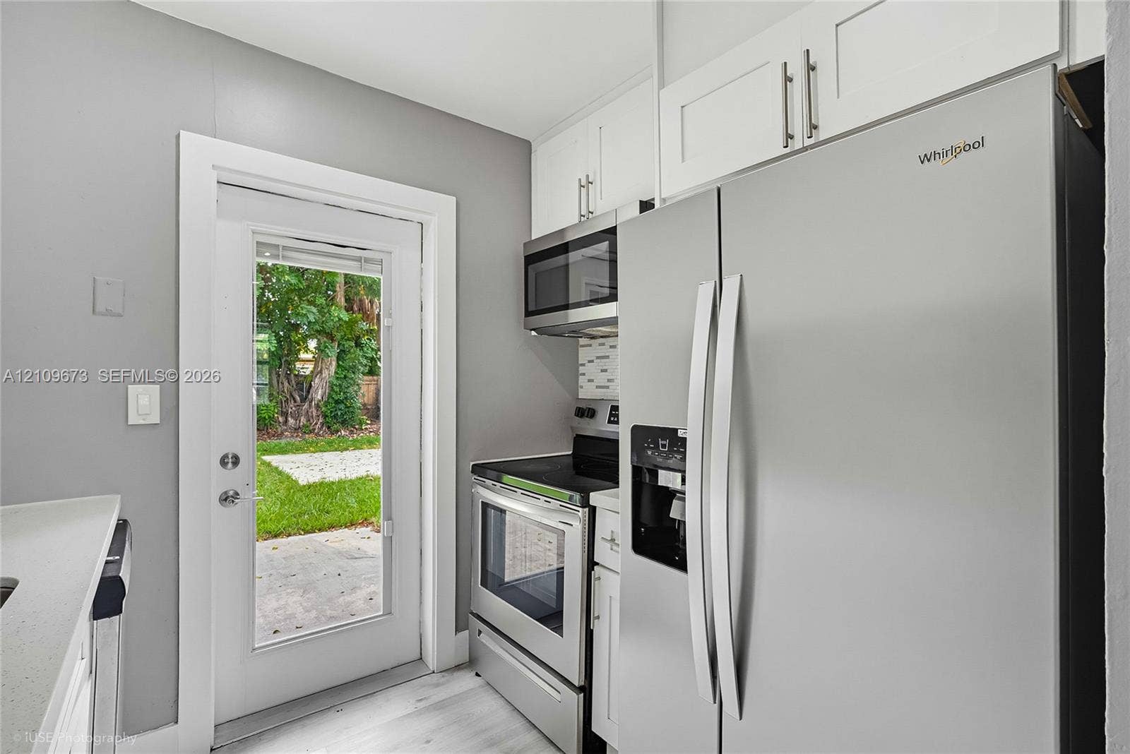 1748 NE 49th Street, Pompano Beach, FL 33064 Kitchen area featuring white shaker-style cabinetry, stainless steel appliances, light-toned wood-finish flooring, and a glass-paneled exterior door